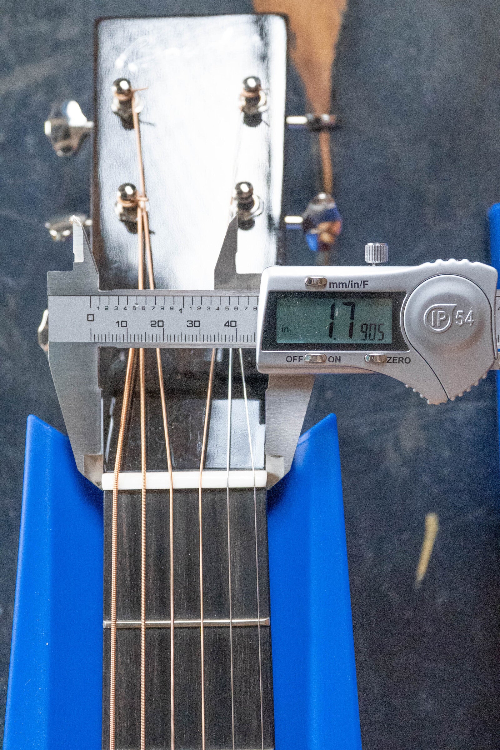 A digital caliper measures the nut width of a *Dread-Not Certified Used* Boucher BG-52-GM Bluegrass Goose Series Dreadnought Acoustic Guitar #1339 at 47.905 mm, with its headstock and strings supported by blue holders.