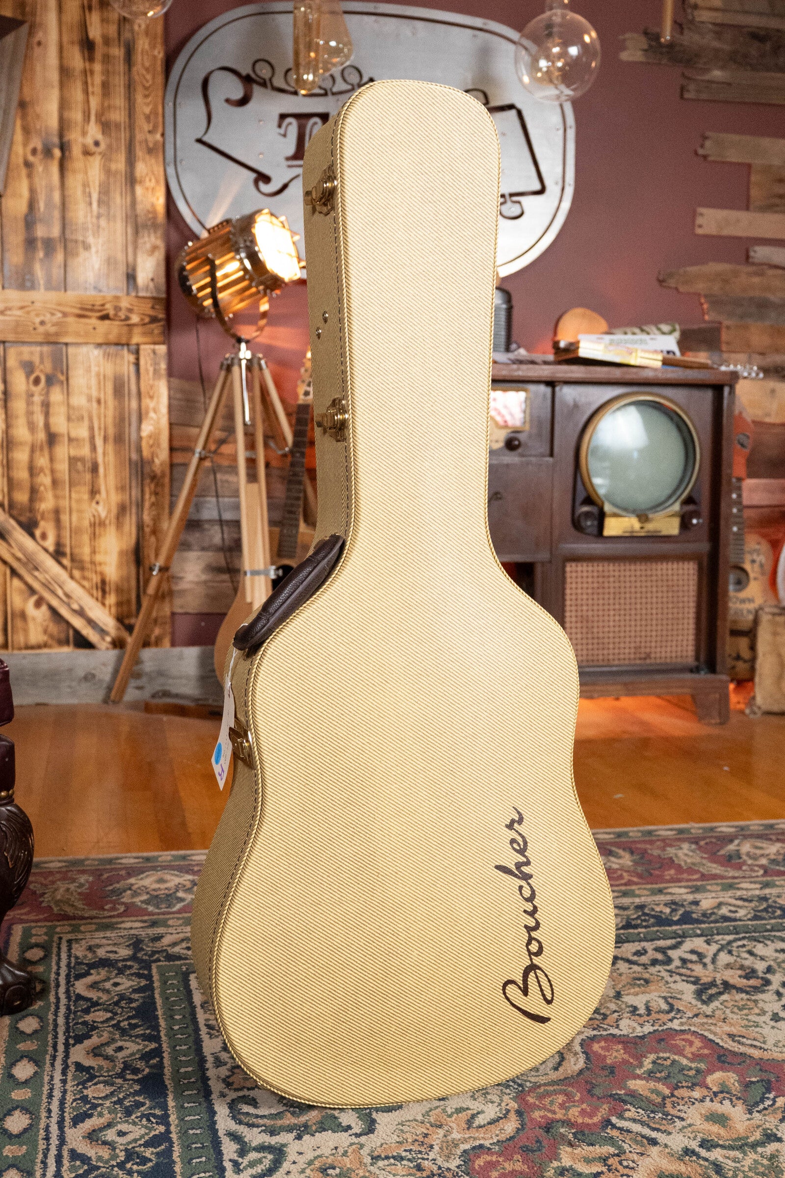 A beige Boucher guitar case stands in a cozy room—perfect for storing your Boucher Guitars *Dread-Not Certified Used* BG-52-GM Torrefied Master Grade Adirondack Red Spruce/East Indian Rosewood Bluegrass Goose Series Dreadnought Acoustic Guitar #1339.