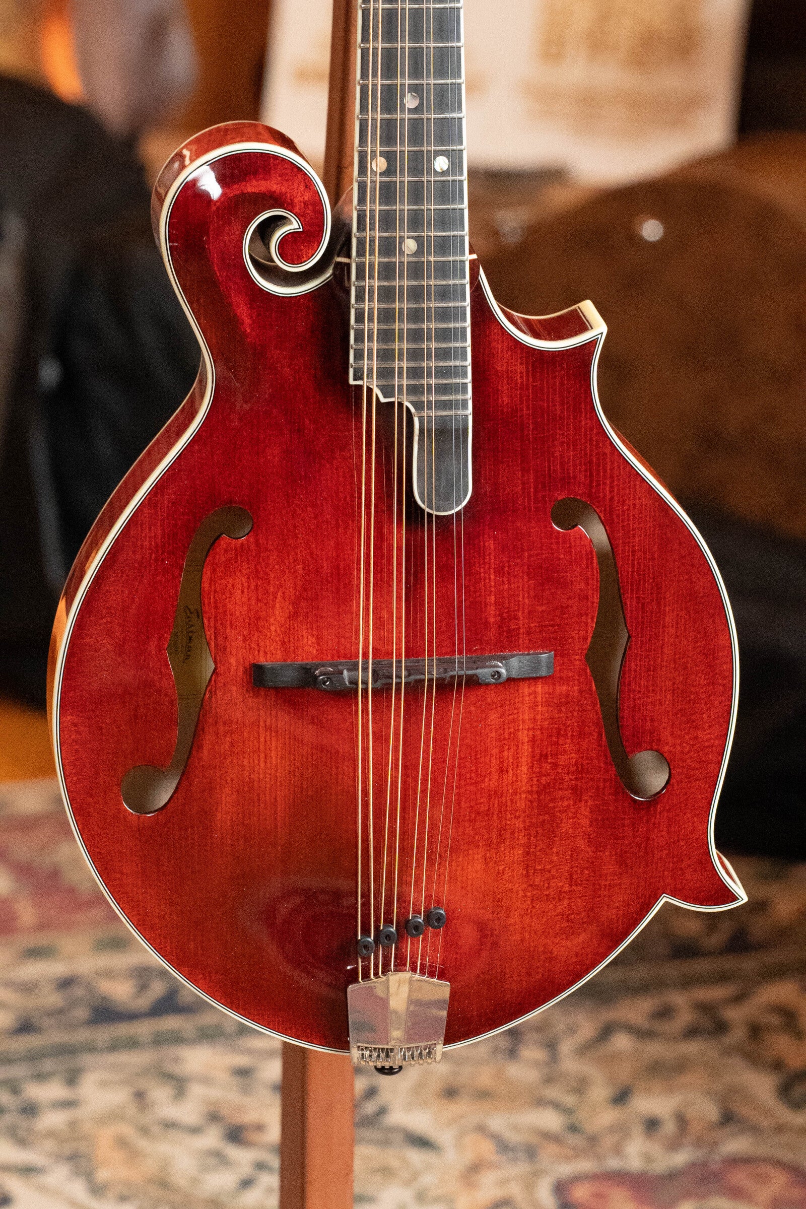 A close-up of a *Dread-Not Certified Used* Eastman Guitars MDA815 F-Style Mandola Classic Finish #4978, featuring a solid spruce top, decorative scroll, and f-holes, standing on a patterned rug.