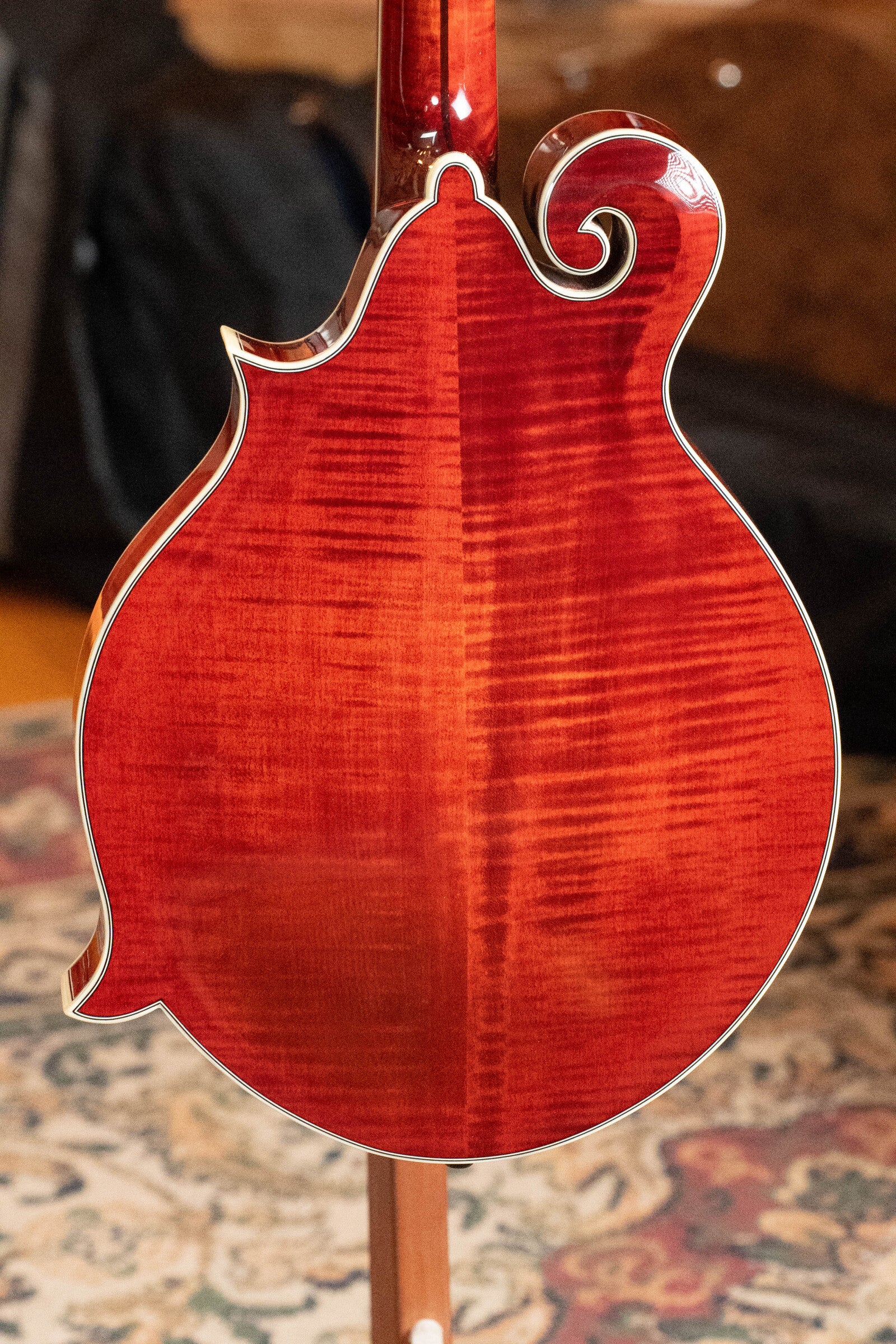 The *Dread-Not Certified Used* Eastman MDA815 F-Style Mandola Classic Finish #4978 by Eastman Guitars features a glossy, flamed wood back and decorative scroll, shown resting on a patterned rug with a blurred background.