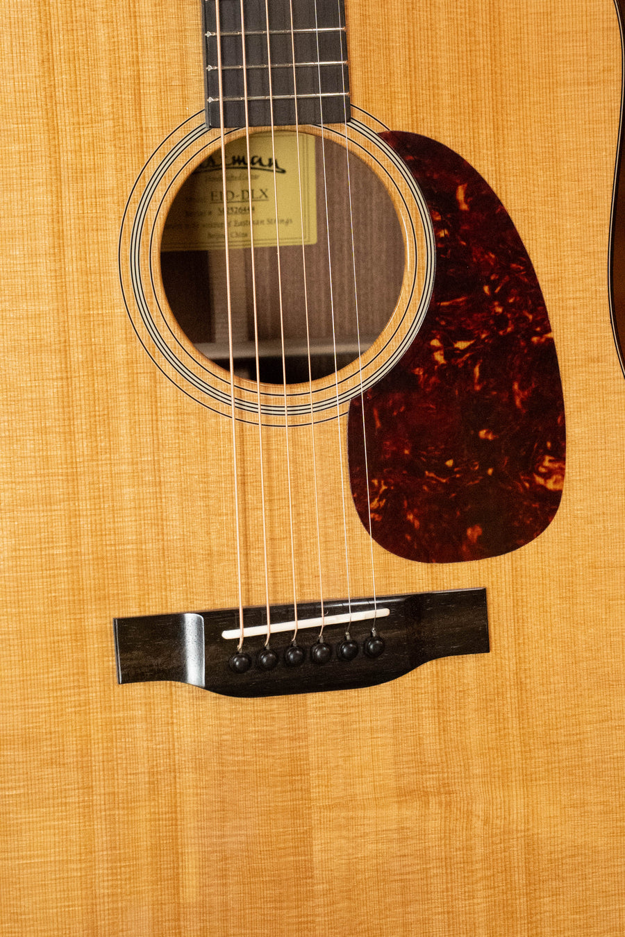 Close-up of the Eastman Guitars E1D-DLX Sitka/Sapele Dreadnought Guitar w/Fishman Pickup #6444, highlighting the sound hole, pickguard, bridge, and six strings on a natural wood grain finish.