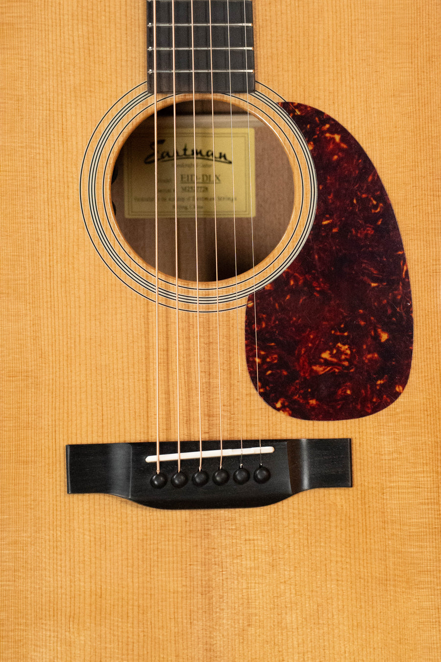Close-up of an Eastman Guitars E1D-DLX Sitka/Sapele Dreadnought Guitar w/Fishman Pickup #7728, showing the sound hole, pickguard, bridge, strings, neck, wood grain, and label inside.