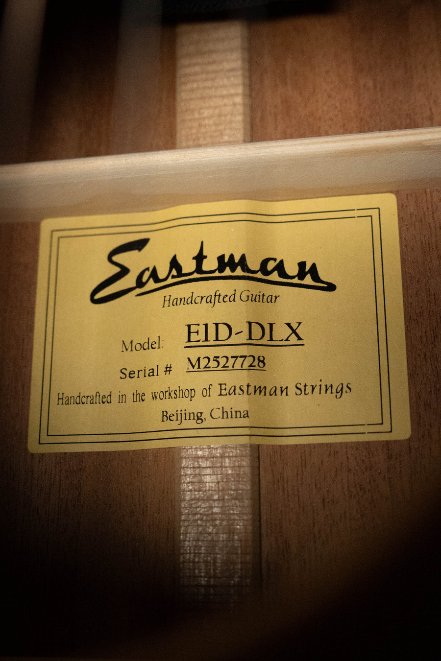 A close-up of a yellow label inside an Eastman Guitars E1D-DLX Sitka/Sapele Dreadnought w/Fishman Pickup #7728, reading: Handcrafted in the workshop of Eastman Strings, Beijing, China.
