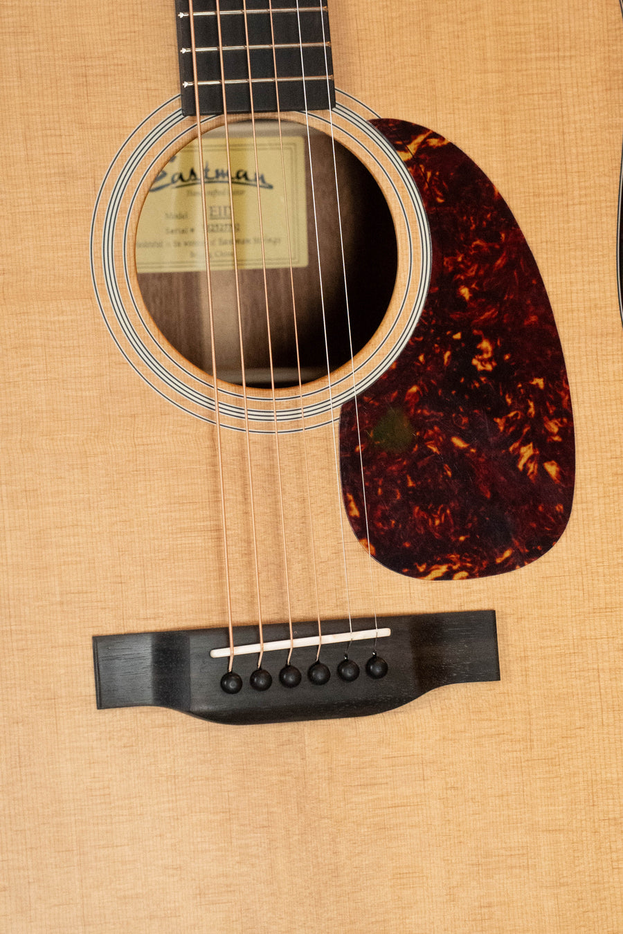 Close-up of the Eastman Guitars E1D Sitka/Sapele Dreadnought Acoustic Guitar #7792 body, showing the sound hole, pickguard, bridge, strings, and label. The top is crafted from beautiful solid Sitka spruce.