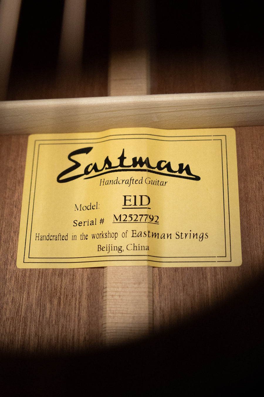 A close-up of a yellow label inside an acoustic guitar reads: Eastman Guitars, E1D Sitka/Sapele Dreadnought Acoustic Guitar #7792. Crafted in Beijing, China, this instrument reflects the quality of Eastman Guitars.