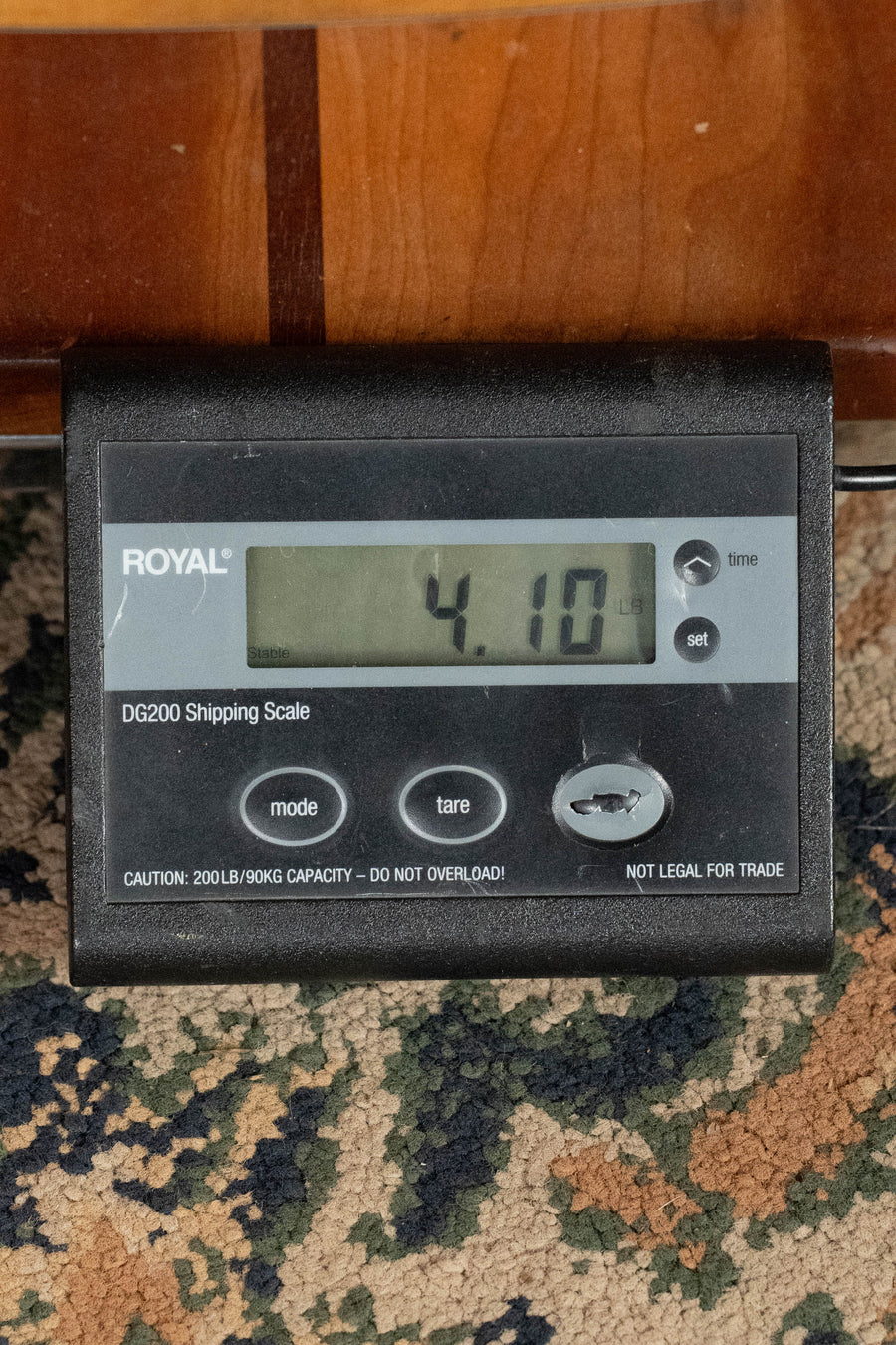 A digital ROYAL DG200 scale on a patterned carpet shows the Eastman Guitars E1D Sitka/Sapele Dreadnought Acoustic Guitar #7792 weighing 4.10 lbs; the scale features mode, tare, and on/off buttons.