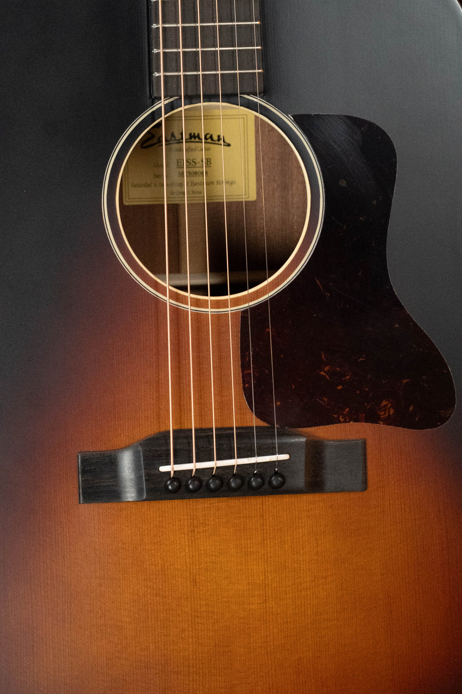 Close-up of the Eastman Guitars E1SS-SB Sitka/Sapele Sunburst Slope Shoulder Dreadnought Acoustic Guitar #8068, showing its richly finished body, sound hole, strings, bridge, pickguard, and label inside.