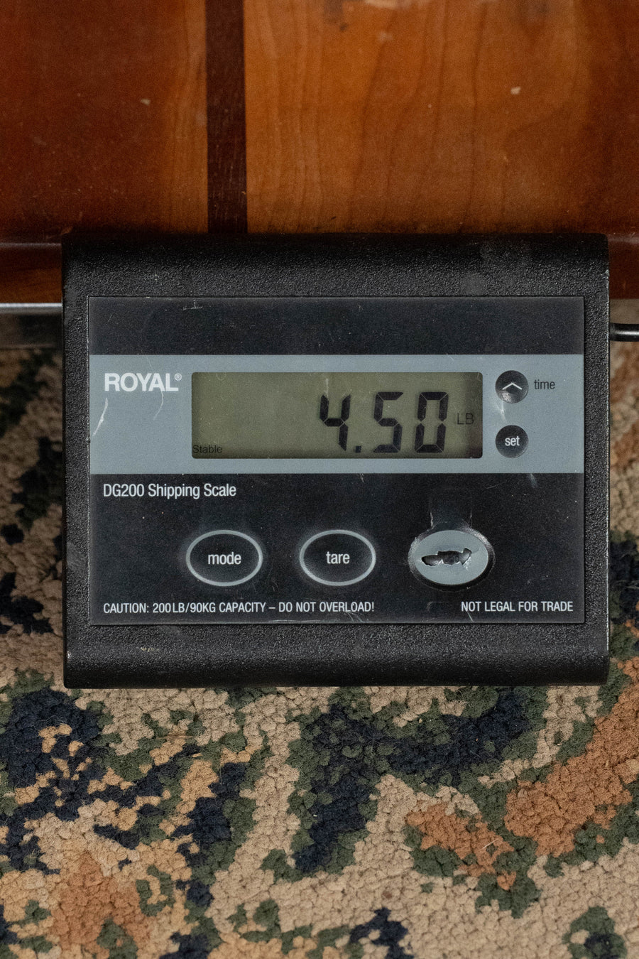 A ROYAL DG200 Shipping Scale on patterned carpet shows 4.50 lbs with the Eastman Guitars E1SS-SB Sitka/Sapele Sunburst Slope Shoulder Dreadnought Acoustic Guitar #8068 resting above it, beneath a wooden surface.
