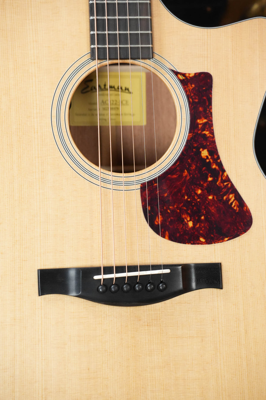 Close-up of an Eastman Guitars AC122-1CE Sitka/Sapele Grand Auditorium Cutaway Guitar (#8979) in a natural finish, showing the soundhole, strings, pickguard, and bridge. The Fishman pickup is included and the guitar label is partially visible inside the soundhole.