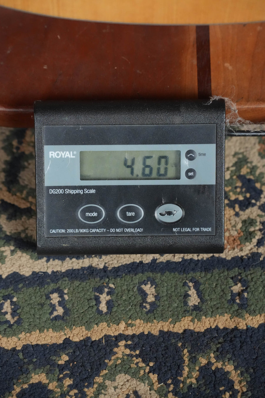 A digital scale on a patterned rug displays 4.60 lbs, with an Eastman Guitars AC122-1CE Sitka/Sapele Natural Finish Grand Auditorium Cutaway Guitar w/Fishman Pickup (#8979) resting partially on top.