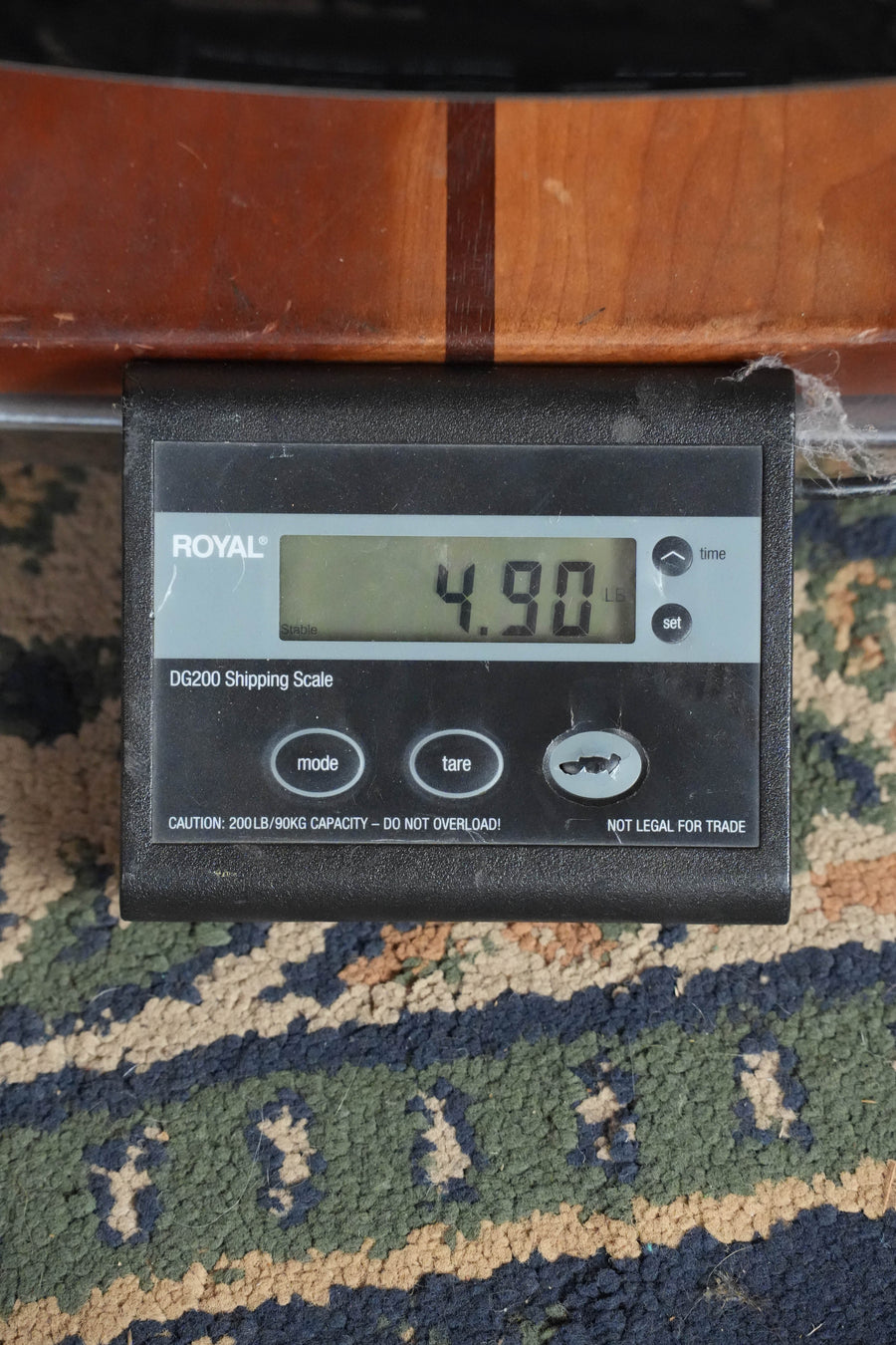 An Eastman AC122-2CE-DLX-SB Cedar/Sapele Sunburst Grand Auditorium Guitar by Eastman Guitars rests on a digital shipping scale displaying 4.90 pounds, placed on a patterned carpet.