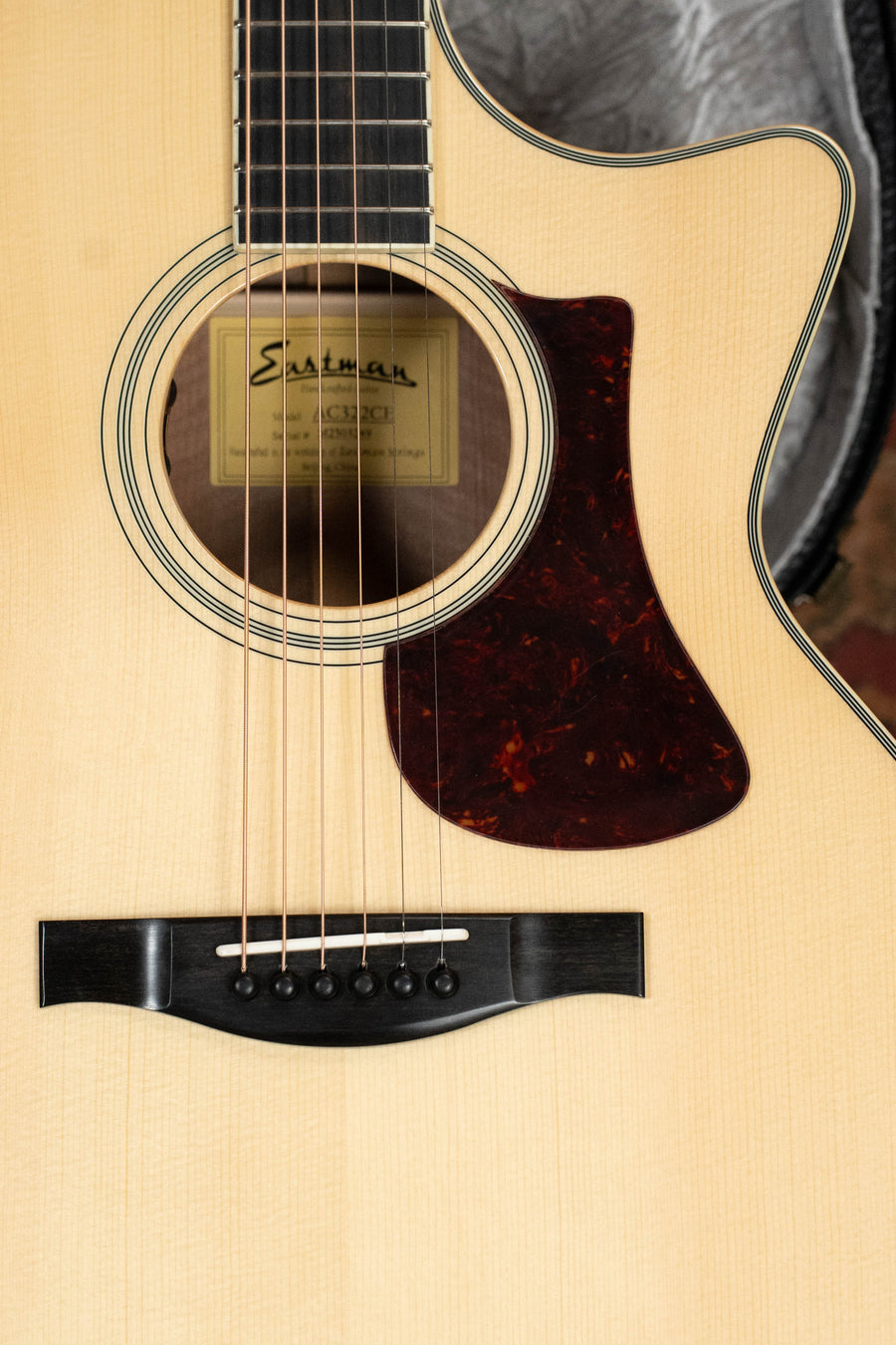 Close-up of the Eastman AC322CE Sitka/Mahogany Grand Auditorium Guitar #3249 by Eastman Guitars, featuring a Sitka Spruce top, sound hole with label, bridge, strings, and tortoiseshell pickguard. Includes LR Baggs pickup.