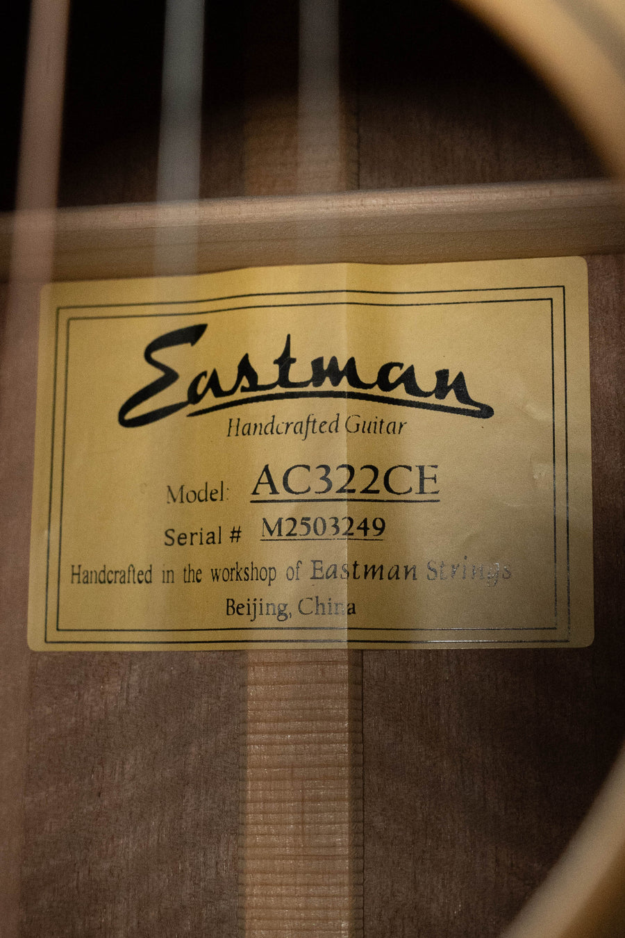 A close-up of the inside label of an Eastman Guitars AC322CE Sitka/Mahogany Cutaway Grand Auditorium (#3249) shows its model, serial number, and handcrafted origin in Beijing, China. Features a solid Sitka spruce top and LR Baggs pickup.
