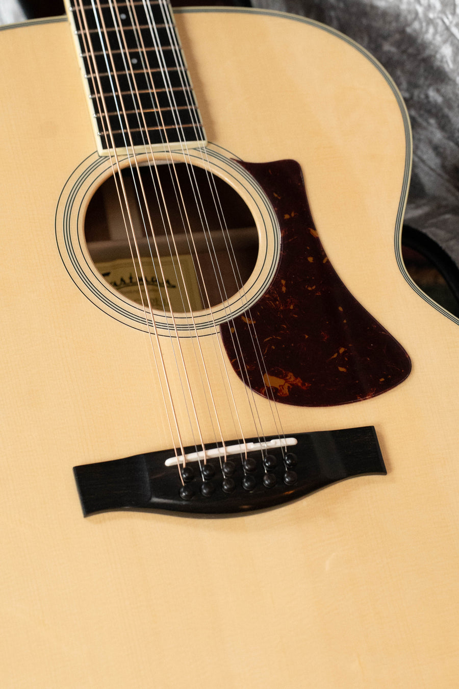 Close-up of an Eastman Guitars AC330E-12 Sitka/Mahogany Jumbo 12-String with LR Baggs Pickup #5666, highlighting the sound hole, strings, pickguard, and bridge on a light wood finish—a beautifully crafted acoustic.
