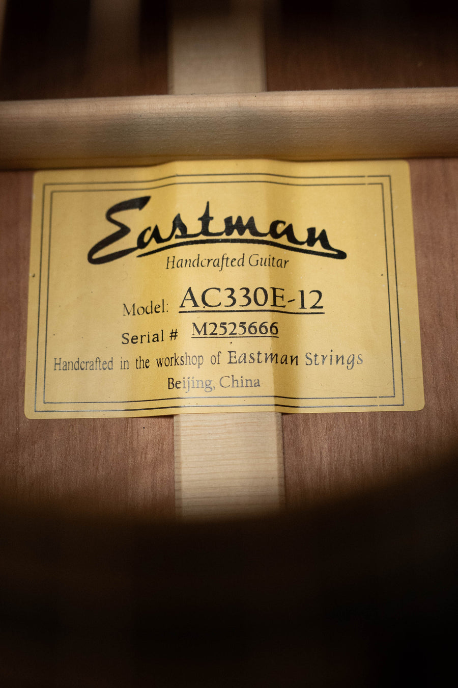 Close-up of a yellow label inside the Eastman Guitars AC330E-12 Sitka/Mahogany Jumbo 12-String Guitar w/LR Baggs Pickup #5666, reading "Eastman Handcrafted Guitar", crafted in Beijing, China.