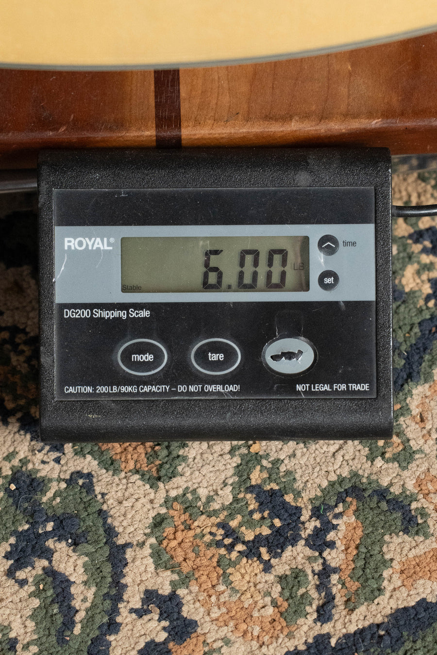 A digital shipping scale (Royal DG200) on a patterned carpet shows 6.00 pounds, with part of an Eastman Guitars AC330E-12 Sitka/Mahogany Jumbo 12-String Guitar w/LR Baggs Pickup (#5666) visible above it.