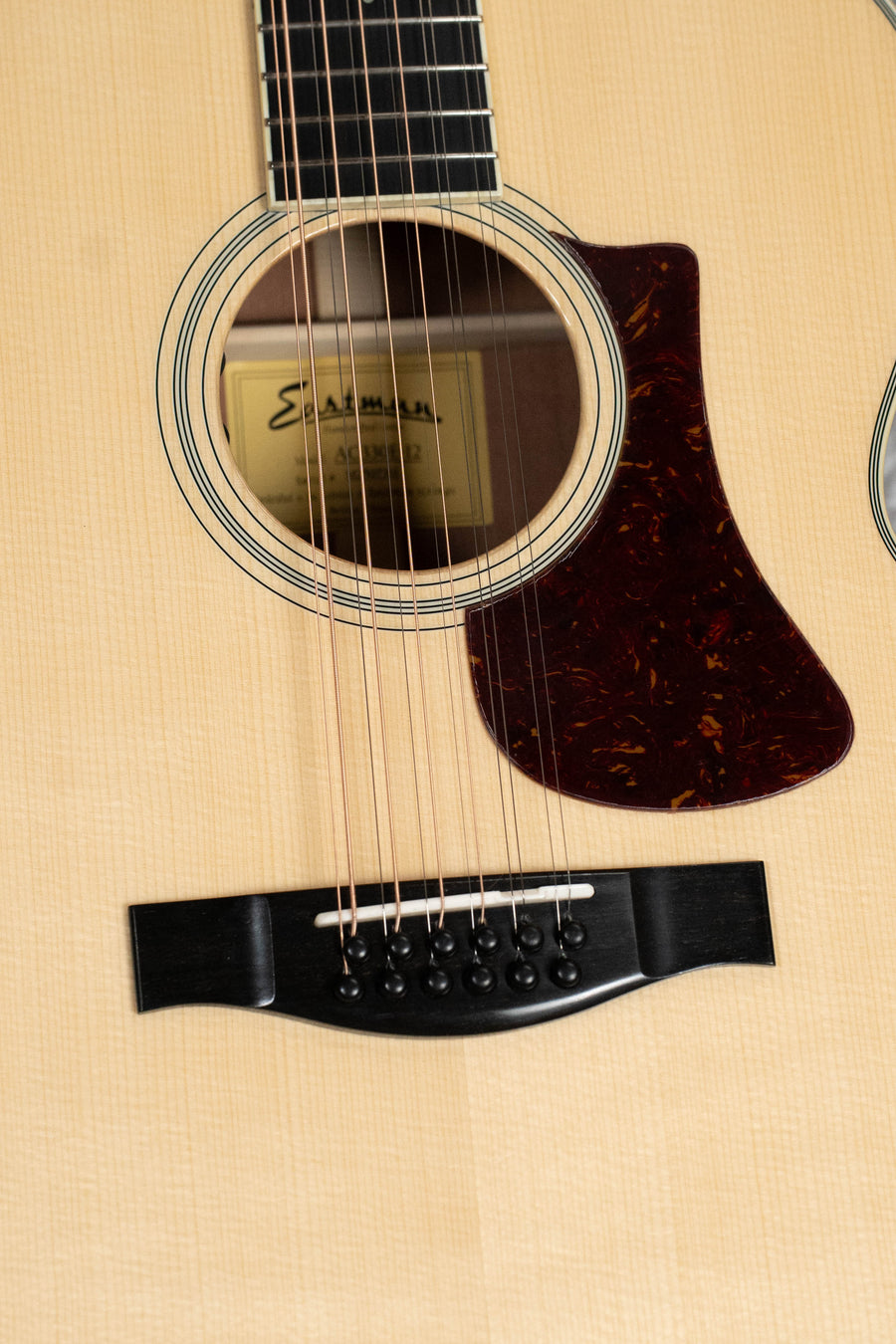 Close-up of the Eastman Guitars AC330E-12 Sitka/Mahogany Jumbo 12-String Guitar w/LR Baggs Pickup, highlighting the sound hole, pickguard, bridge, and strings. The light wood finish and interior label are clearly visible.