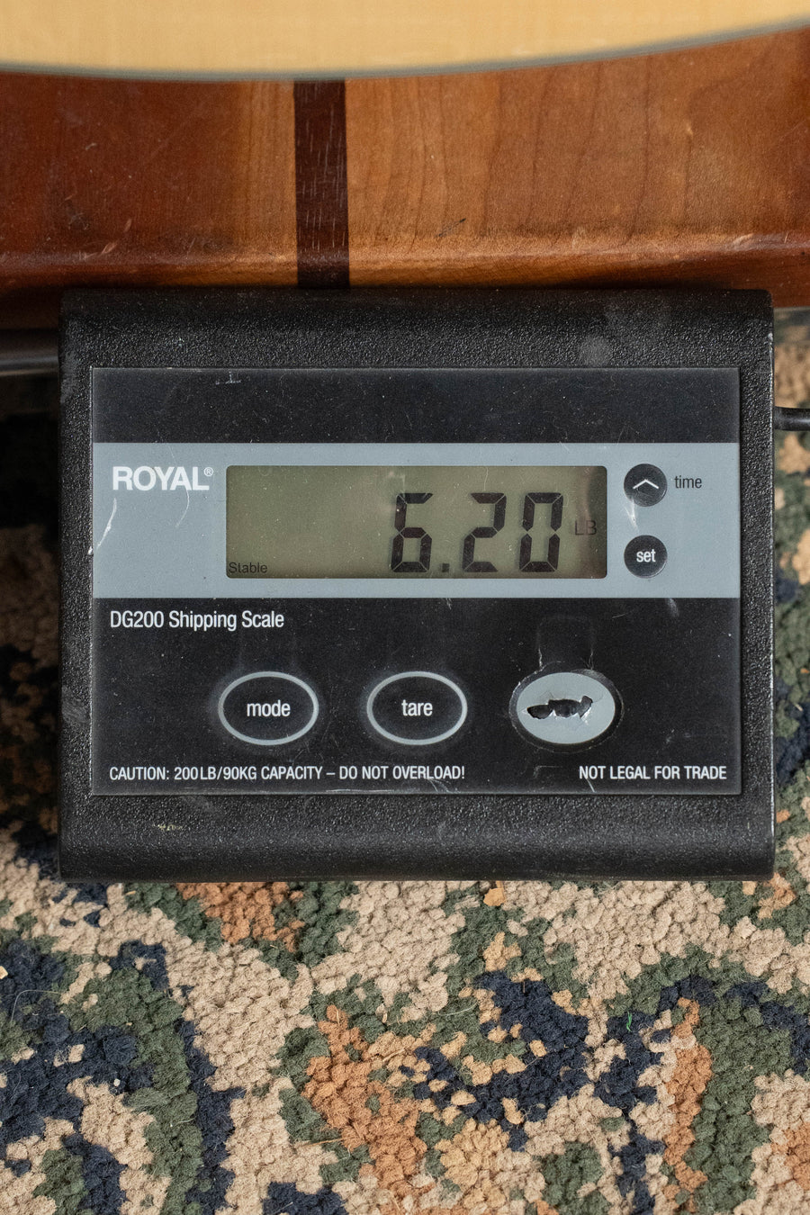 A digital shipping scale on a patterned carpet shows 6.20 lbs, with part of an Eastman Guitars AC330E-12 Sitka/Mahogany Jumbo 12-String Guitar w/LR Baggs Pickup (#7301) visible above it.