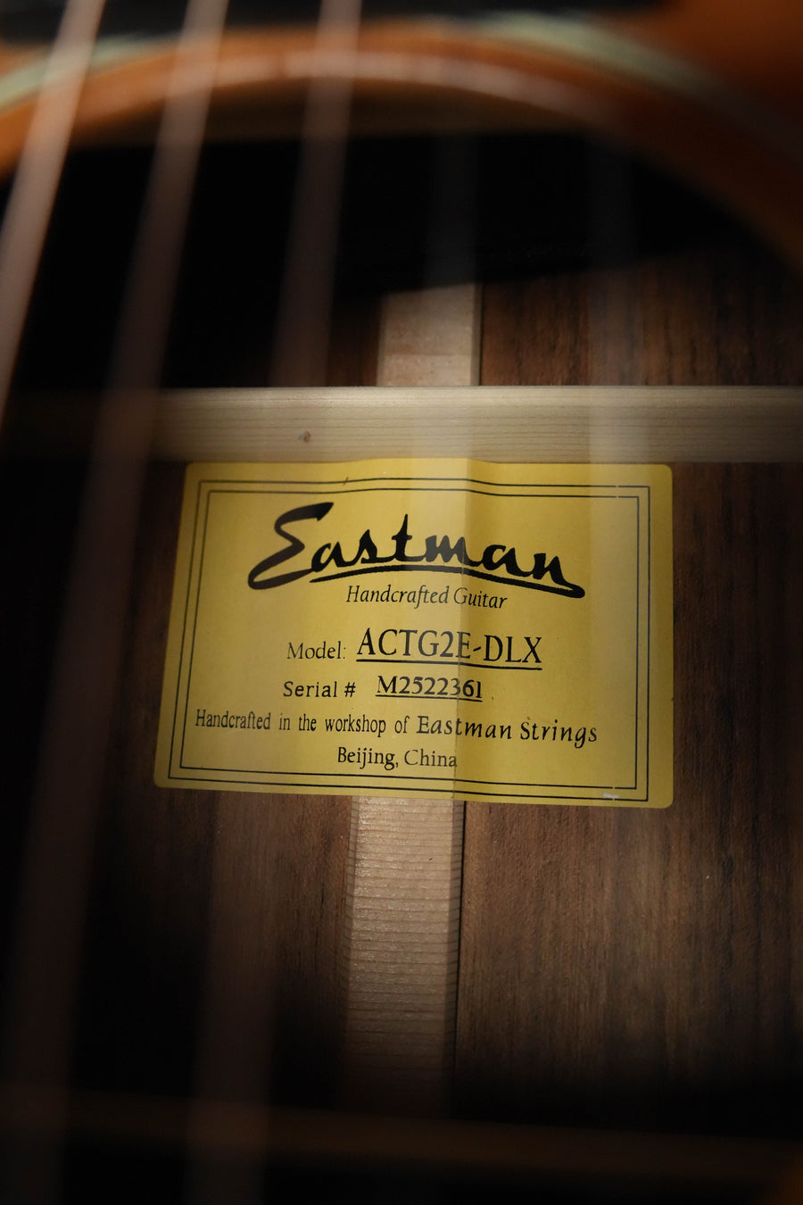 Close-up of a label inside an Eastman Guitars ACTG2E-DLX Sitka/Ovangkol Travel Guitar w/Fishman Pickup #2361. Guitar strings and the Fishman Presys VT pickup are visible in the foreground.