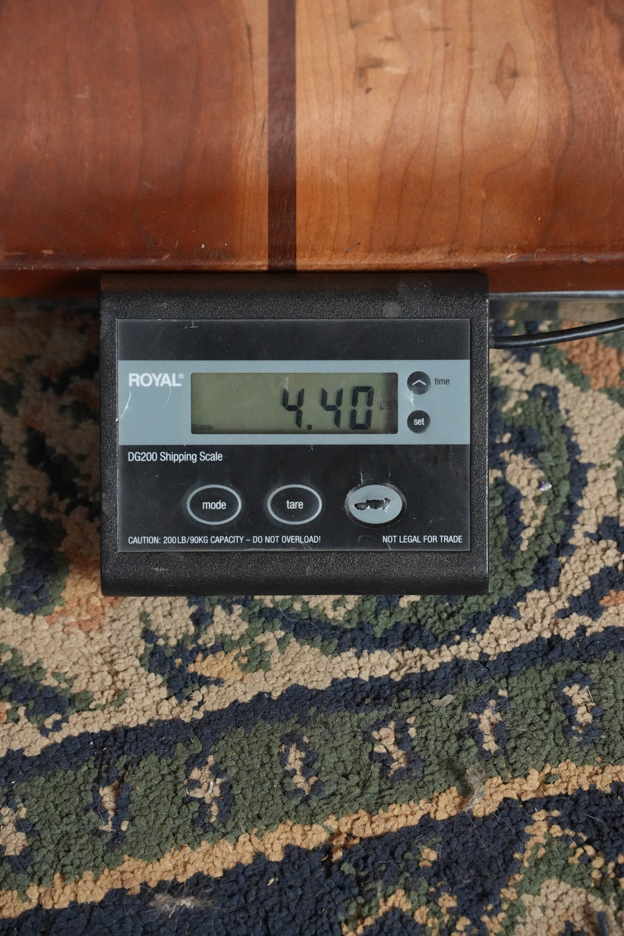 A digital shipping scale shows 4.40 pounds on a patterned carpet, with an Eastman Guitars ACTG2E-DLX Sitka/Ovangkol Travel Guitar w/Fishman Pickup (#2361) partially visible resting on top.