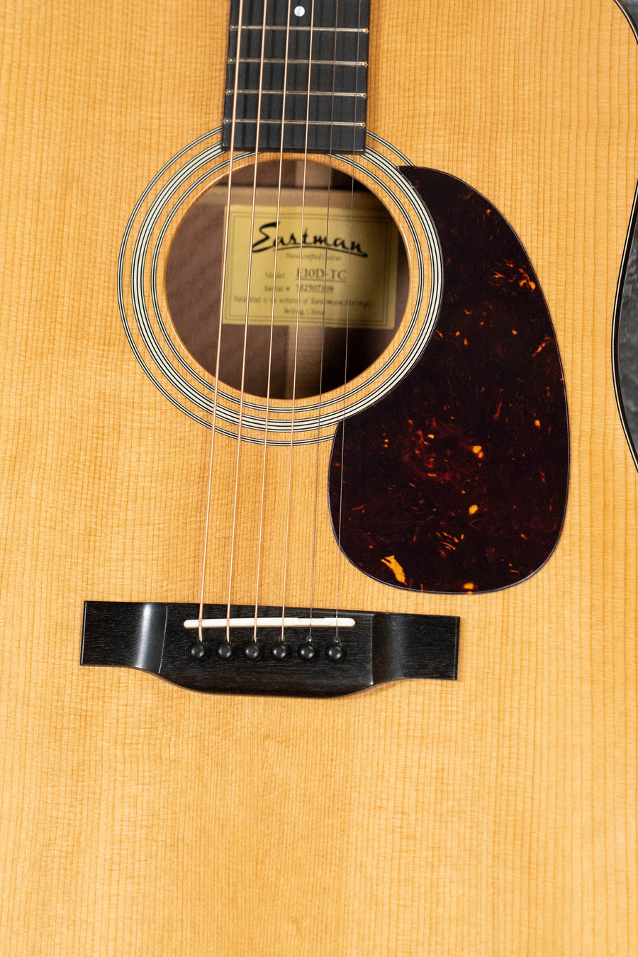 Close-up of the Eastman Guitars E10D-TC Thermo-Cured Adirondack/Mahogany Dreadnought Acoustic Guitar #7309, showing its light wood body, dark pickguard, visible strings, and label inside the sound hole for a vintage-inspired look.