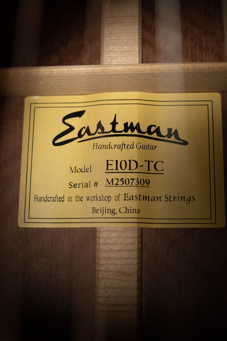 A yellow label inside an Eastman Guitars E10D-TC Thermo-Cured Adirondack/Mahogany Dreadnought Acoustic Guitar #7309 notes its handcrafted, vintage-inspired tone and origins in Beijing, China.
