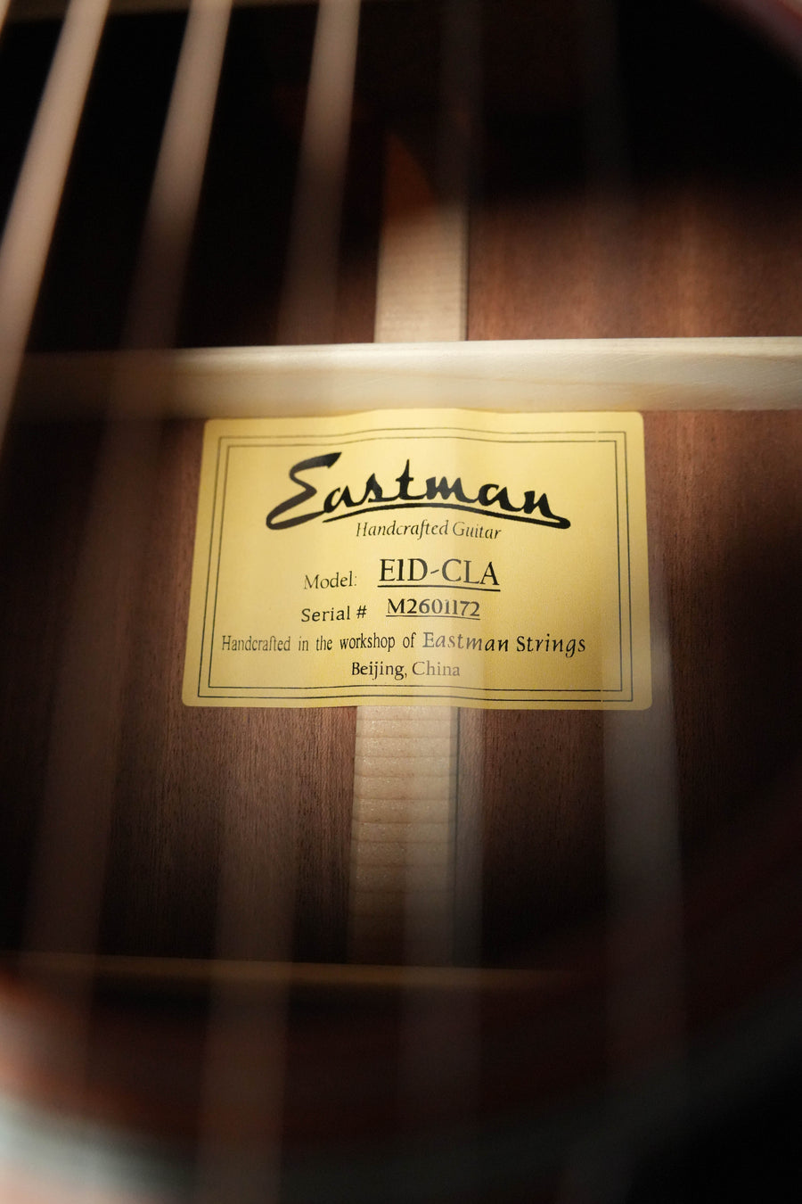 Close-up of the guitar’s interior with a yellow label reading: “Eastman Guitars, E1D-CLA Classic Finish Dreadnought Acoustic Guitar #1173, solid Sitka spruce top, handcrafted in Beijing, China.”.