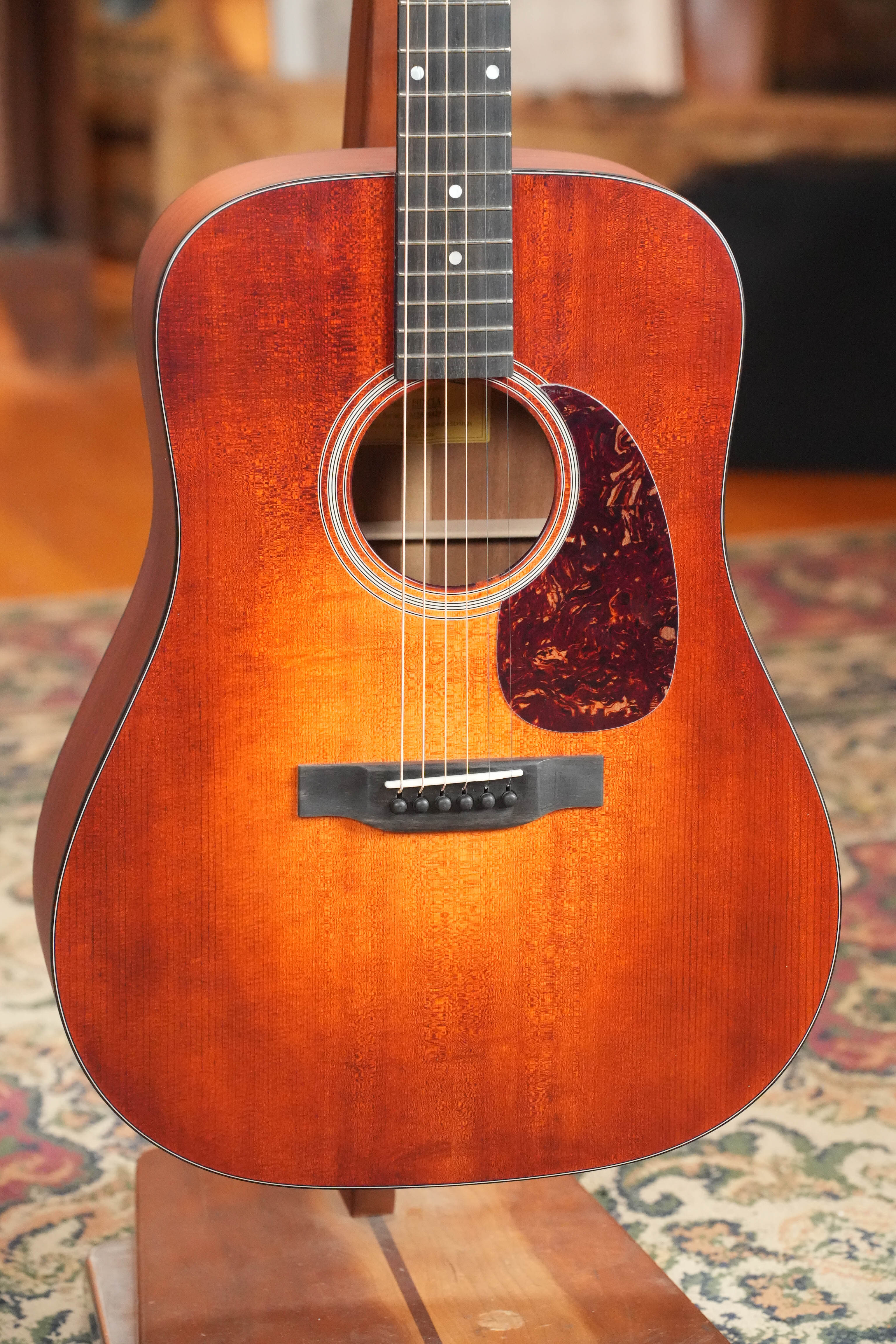 A close-up of the Eastman Guitars E1D-CLA Classic Finish Dreadnought Acoustic Guitar #9429 with solid Sitka spruce top, pickguard, and fretboard, displayed on a wooden stand over a patterned rug.