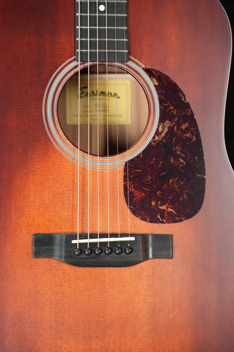 Close-up of the Eastman Guitars E1D-CLA Classic Finish Dreadnought Acoustic Guitar #9747, showing its warm brown solid Sitka spruce top, sound hole, black six-pin bridge, strings, tortoiseshell pickguard, and interior label.