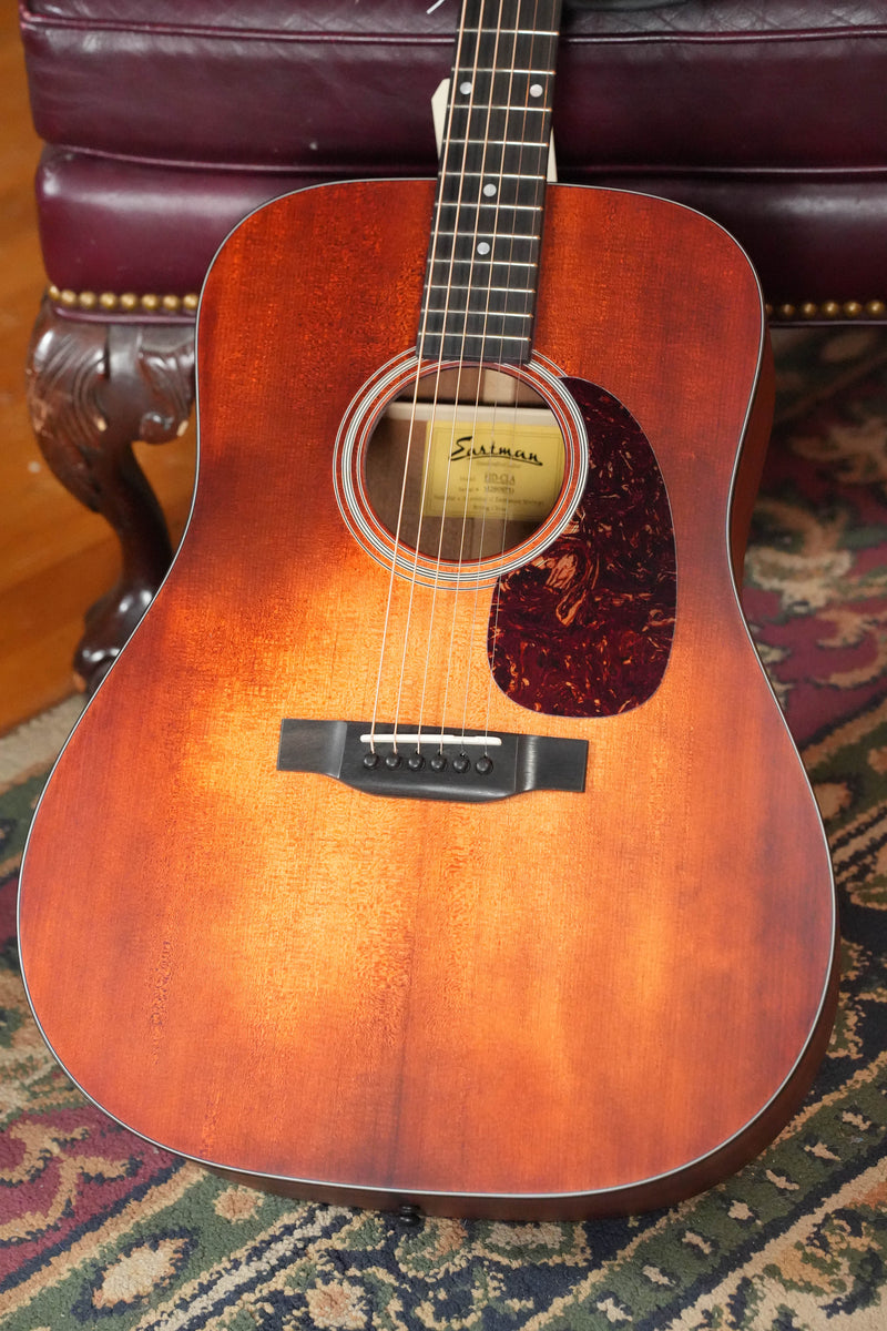 An Eastman E1D-CLA Classic Finish Dreadnought Acoustic Guitar #9753 from Eastman Guitars, with a solid Sitka spruce top and hand-scalloped X-bracing, rests on a patterned rug in front of a dark red tufted leather chair.
