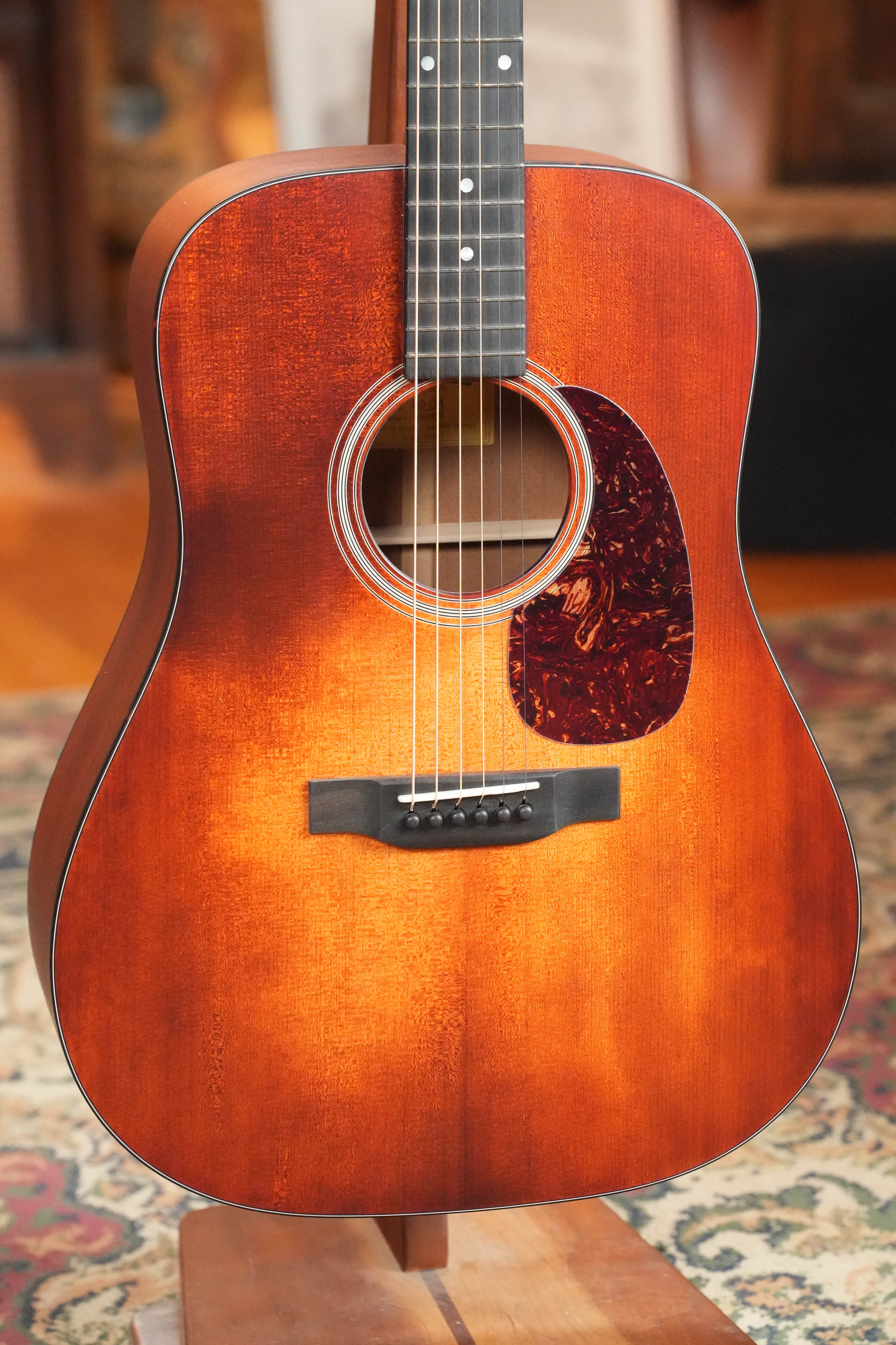 A close-up of the Eastman Guitars E1D-CLA Classic Finish Dreadnought Acoustic Guitar #9753, featuring a sunburst finish and black pickguard, standing upright on a wooden floor with a patterned rug in the background.