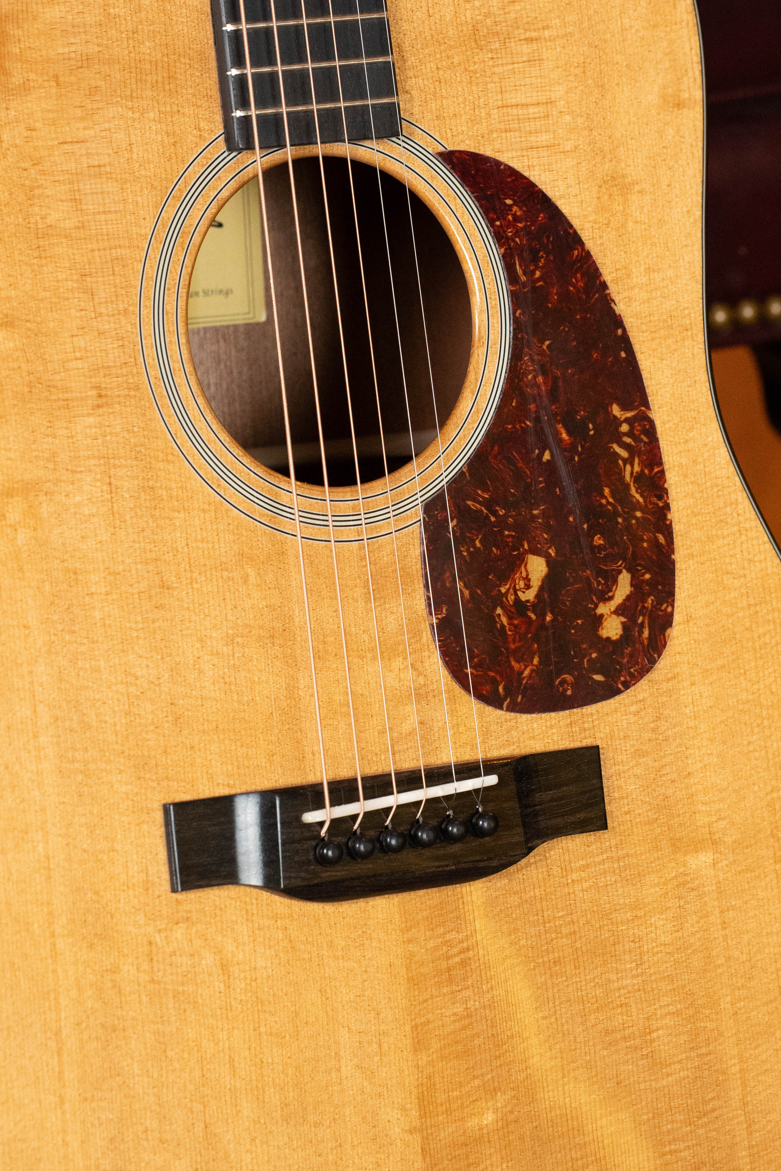 Close-up of the Eastman Guitars E1D-DLX Sitka/Sapele Dreadnought Guitar w/Fishman Pickup #5656, highlighting its sound hole, pickguard, strings, and bridge on a natural wood finish.