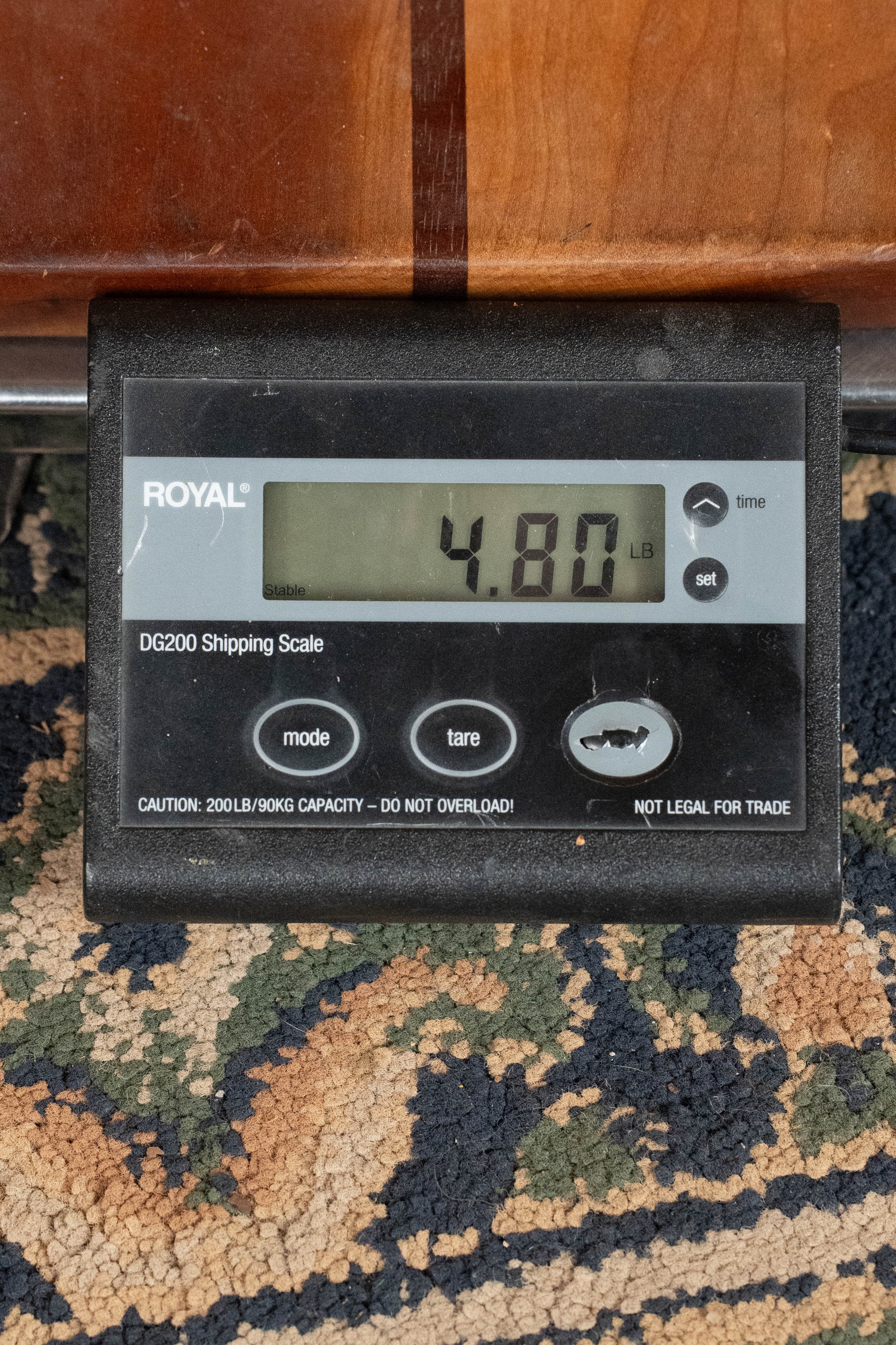 A digital shipping scale shows 4.80 pounds. The black scale is on patterned carpet, with an Eastman Guitars E1D-DLX Sitka/Sapele Dreadnought Guitar w/Fishman Pickup (#5656) visible on a wooden surface above it.