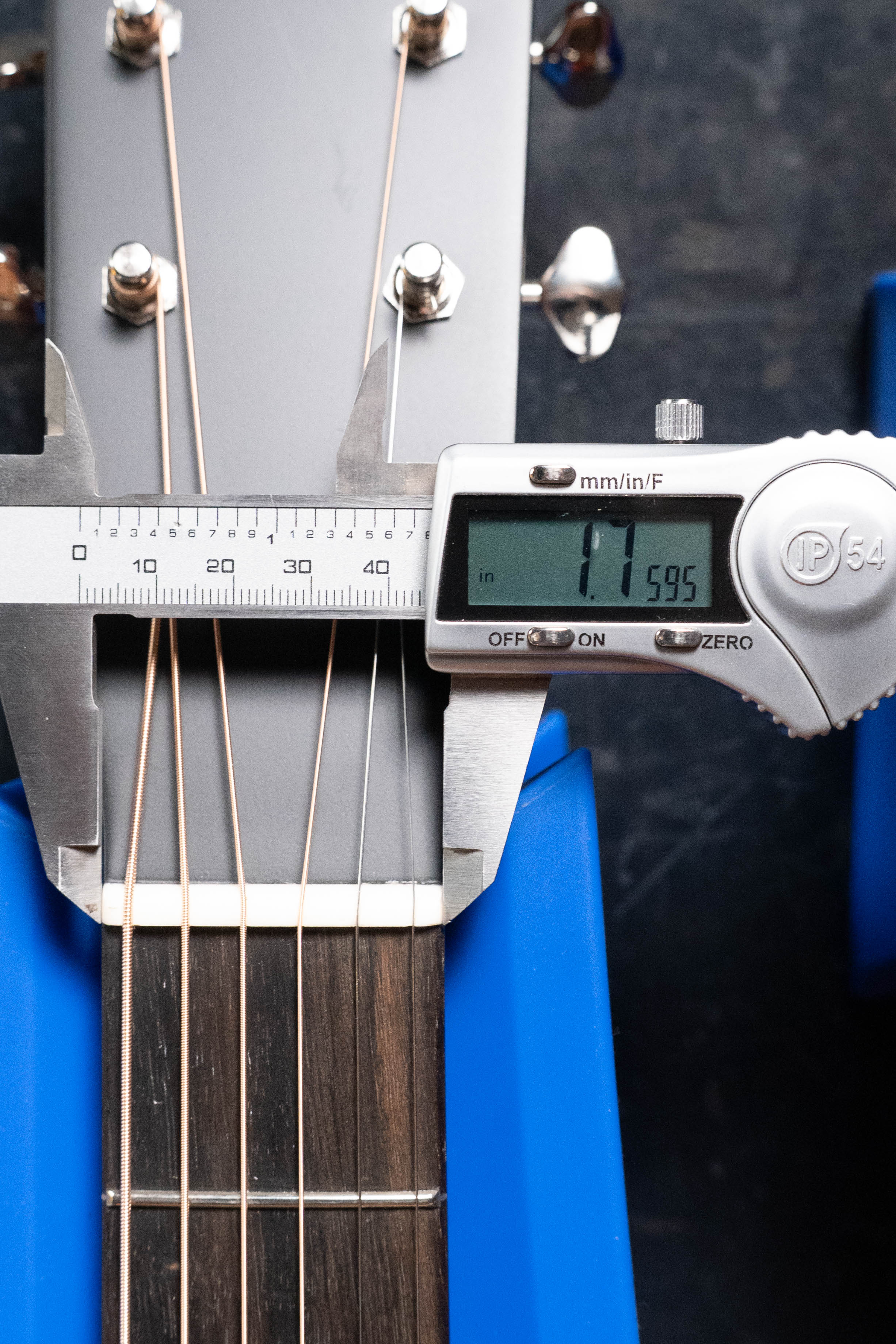 Digital calipers show the Eastman Guitars E1D-DLX Sitka/Sapele Dreadnought Guitar w/Fishman Pickup #7721 neck width at the nut as 1.595 inches. The solid Sitka spruce top guitar rests securely in blue supports.