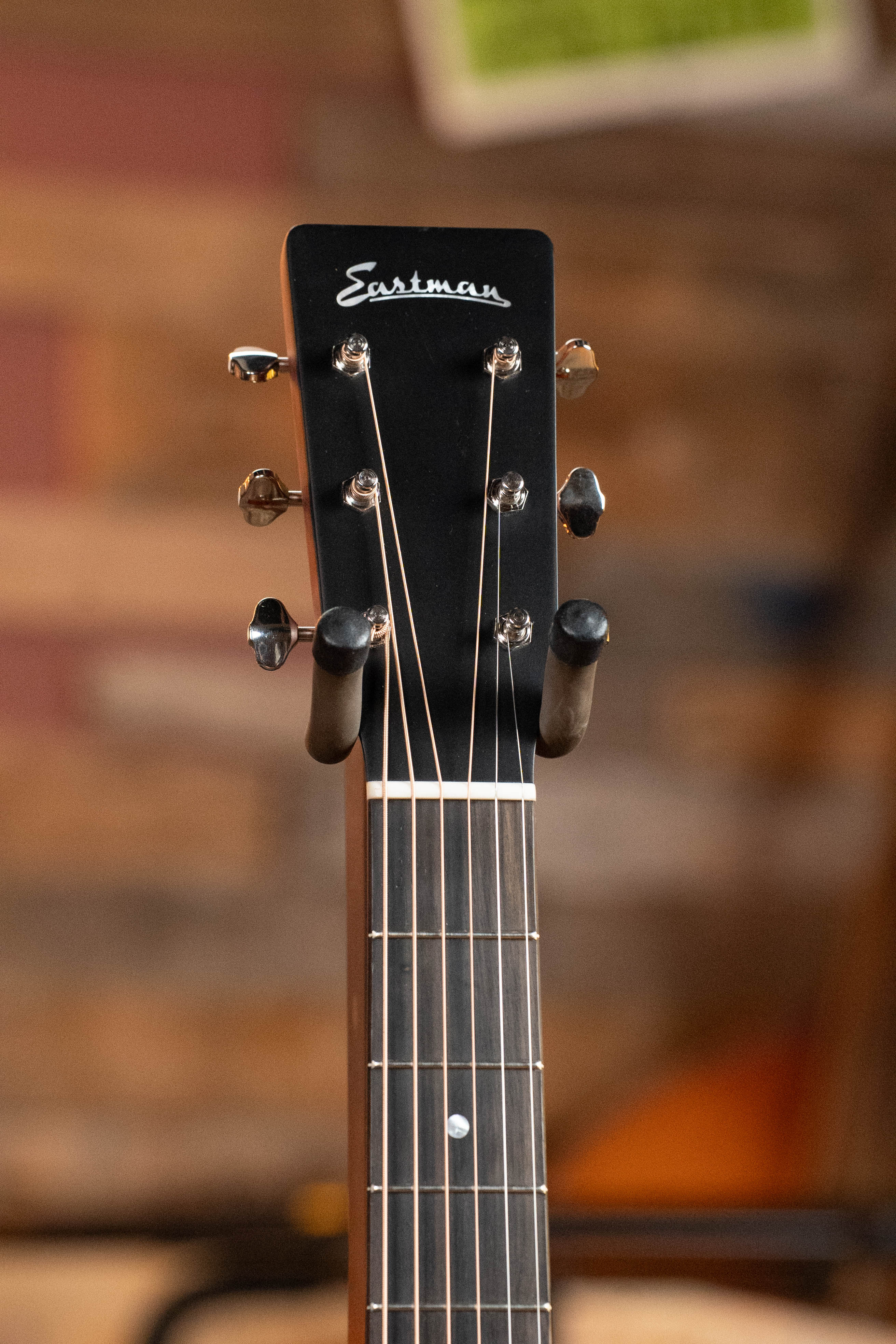 Close-up of the headstock of an Eastman Guitars E1D-DLX Sitka/Sapele Dreadnought Guitar w/Fishman Pickup #7721, highlighting tuning pegs and strings, set against a blurred background of wooden panels.