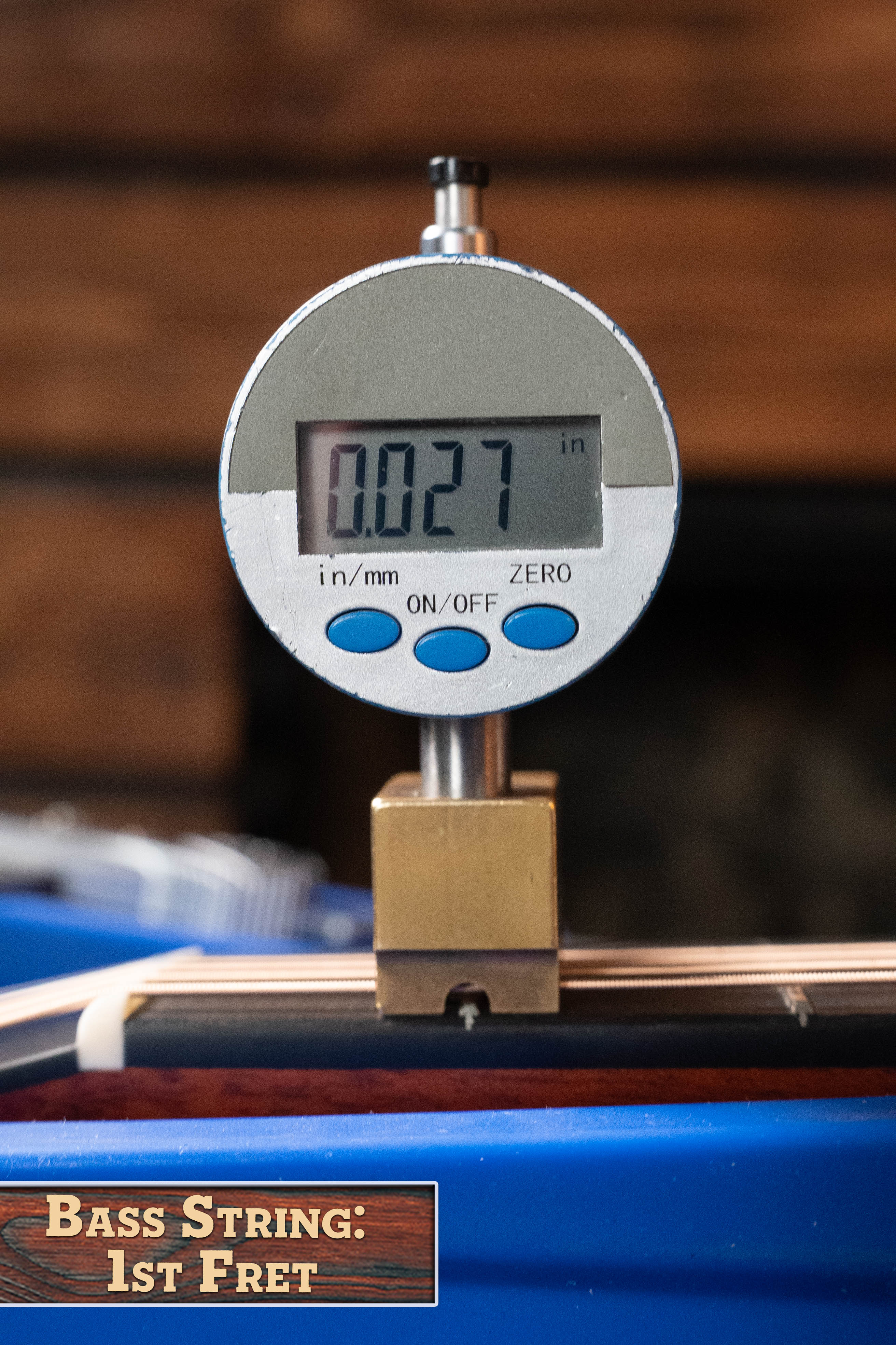 A digital gauge shows 0.027 inches measuring string height at the first fret, like setting up an Eastman Guitars E1D-DLX Sitka/Sapele Dreadnought w/Fishman Pickup #7721. Label reads: BASS STRING: 1ST FRET.