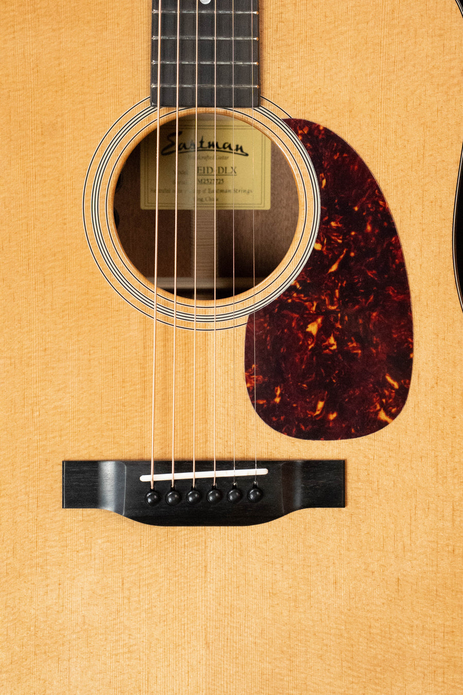 Close-up of the Eastman Guitars E1D-DLX Sitka/Sapele Dreadnought (#7725) showing strings, sound hole with "Eastman" label, bridge, and pickguard. Features a light natural finish and includes a Fishman pickup.