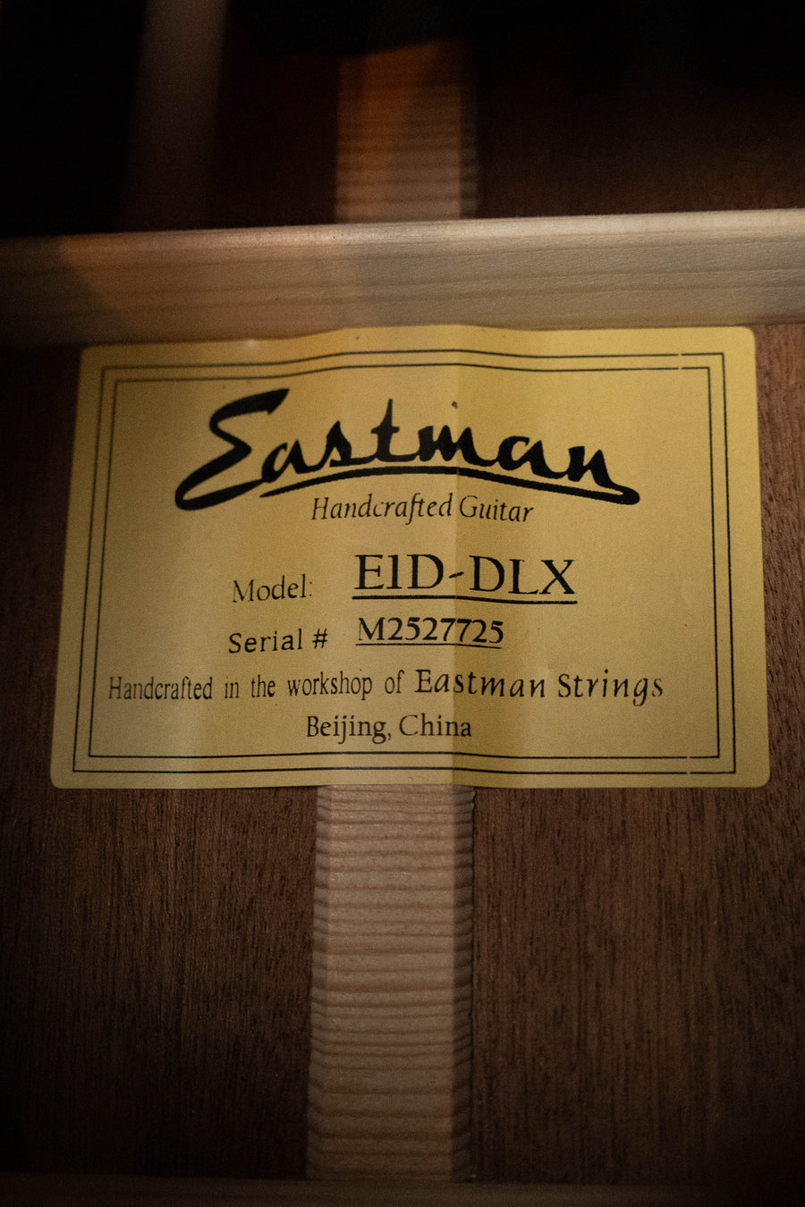 A yellow label inside the wooden dreadnought reads: “Eastman Guitars E1D-DLX Sitka/Sapele w/Fishman Pickup #7725. Handcrafted in the workshop of Eastman Strings, Beijing, China.”.