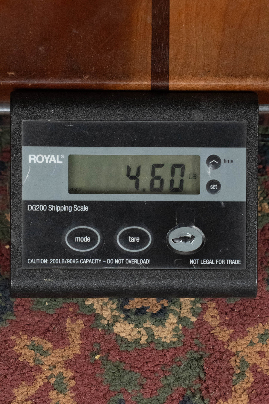 A digital shipping scale on a patterned carpet shows 4.60 lbs—perfect for sending an Eastman Guitars E1D-DLX Sitka/Sapele Dreadnought w/Fishman Pickup #7725. The scale offers mode, tare, arrow buttons, and a weight capacity warning.