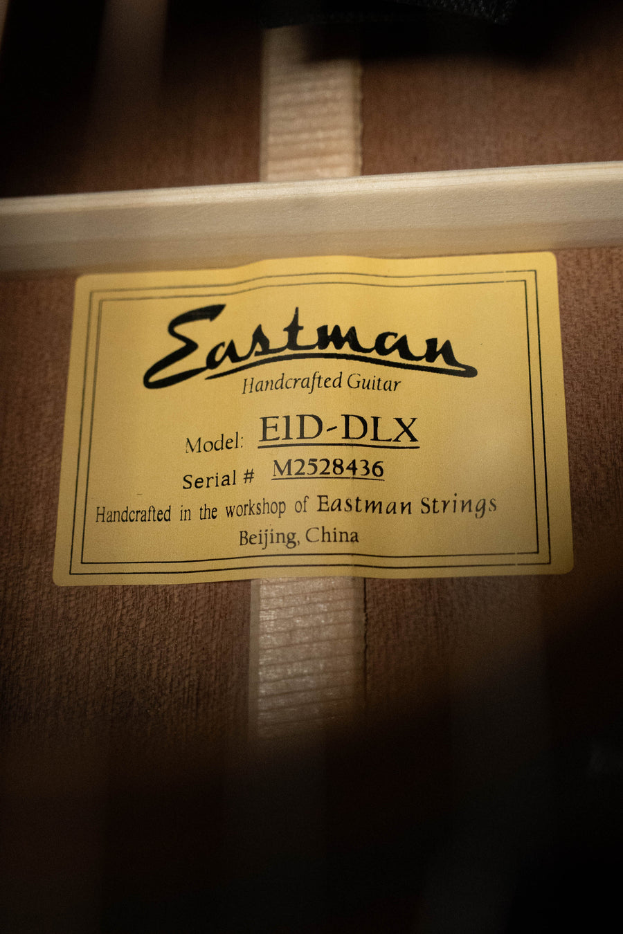 A yellow label inside the wooden dreadnought reads: Eastman Guitars Handcrafted Guitar, Model: E1D-DLX Sitka/Sapele w/Fishman Pickup #8436, made in the workshop of Eastman Guitars, Beijing, China.