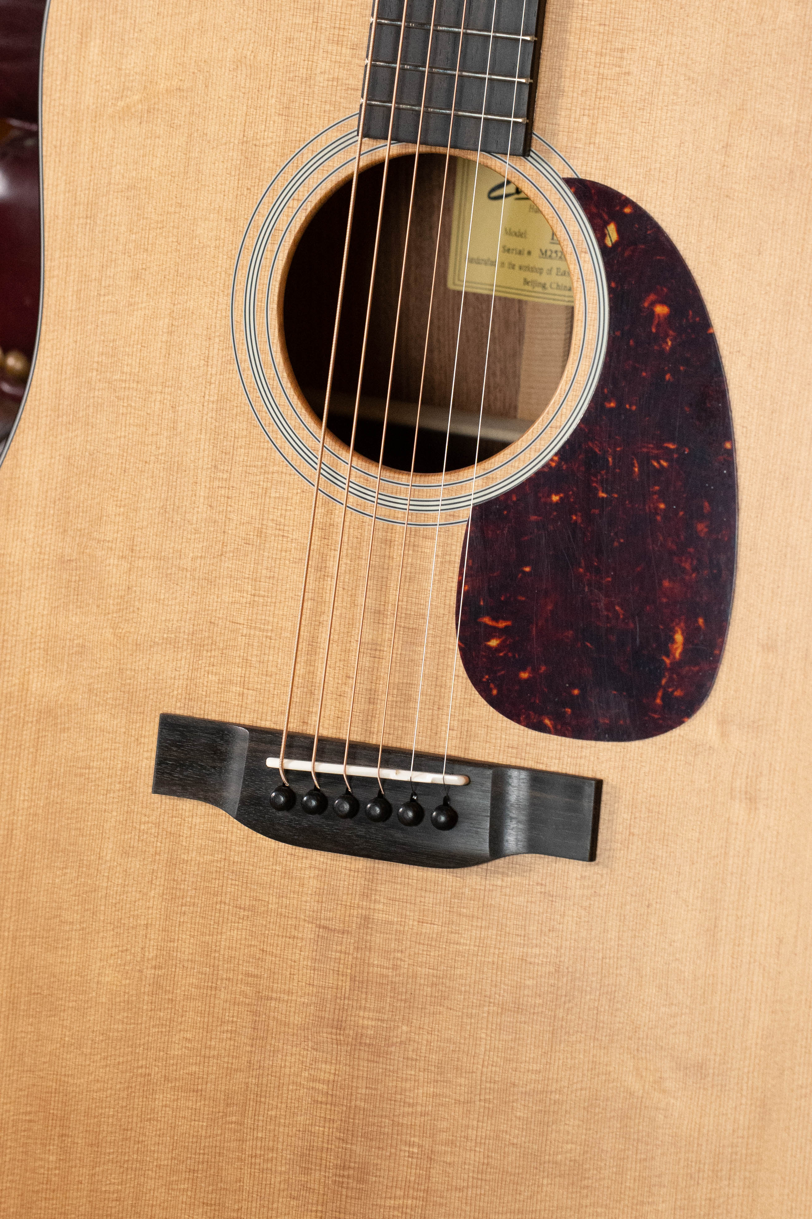 Close-up of the Eastman Guitars E1D Sitka/Sapele Dreadnought Acoustic Guitar #6855, highlighting the sound hole, pickguard, bridge, strings, and visible solid Sitka spruce wood grain with a partially seen label inside the sound hole.