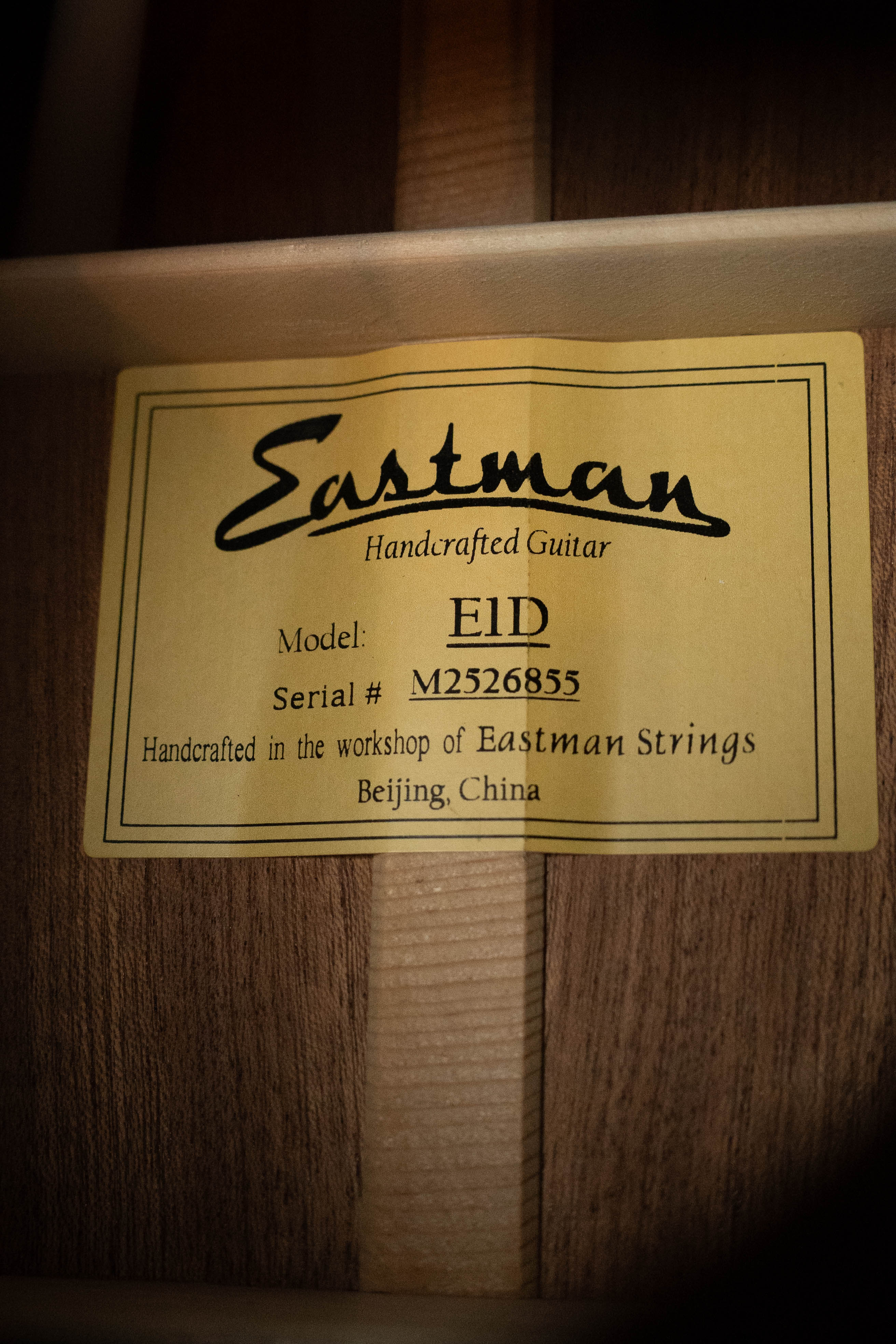 A yellow label inside the Eastman Guitars E1D Sitka/Sapele Dreadnought Acoustic Guitar #6855 notes it’s handcrafted in Beijing, China, featuring a solid Sitka spruce top, and marked as Model E1D with Serial #M2526855.