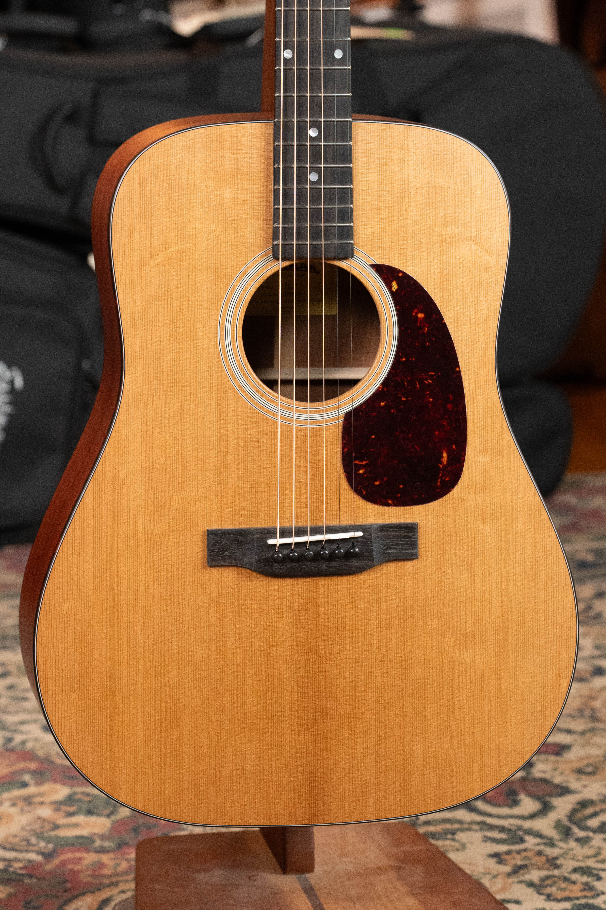 A close-up of the Eastman Guitars E1D Sitka/Sapele Dreadnought Acoustic Guitar #6855, featuring a natural solid Sitka spruce top, dark pickguard, and six strings, on a wooden stand over a patterned rug in soft focus.