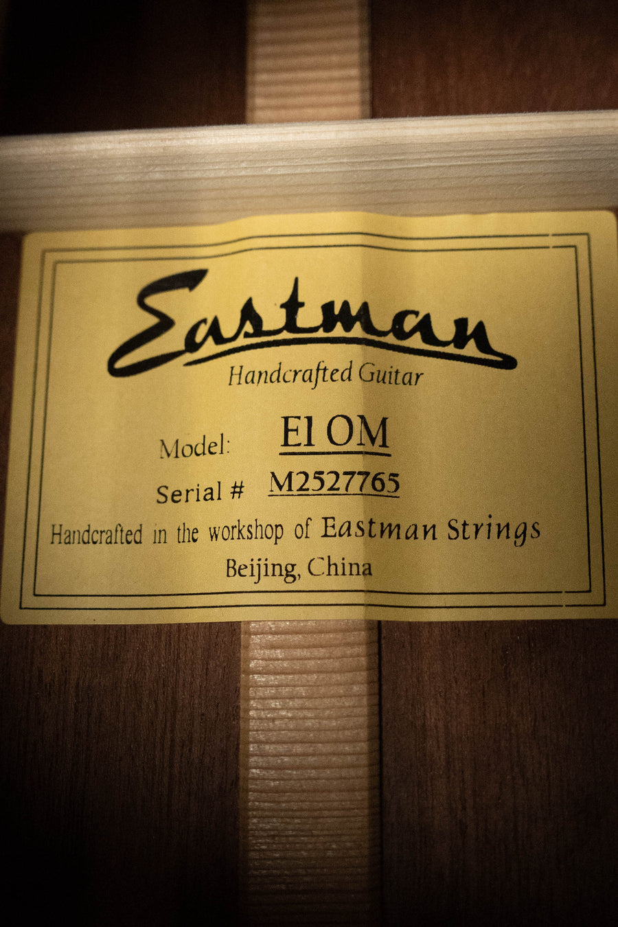 A yellow label inside this acoustic guitar reads: Eastman Guitars E1OM All Solid Sitka/Sapele Acoustic Guitar #7765. Handcrafted in Beijing, China.