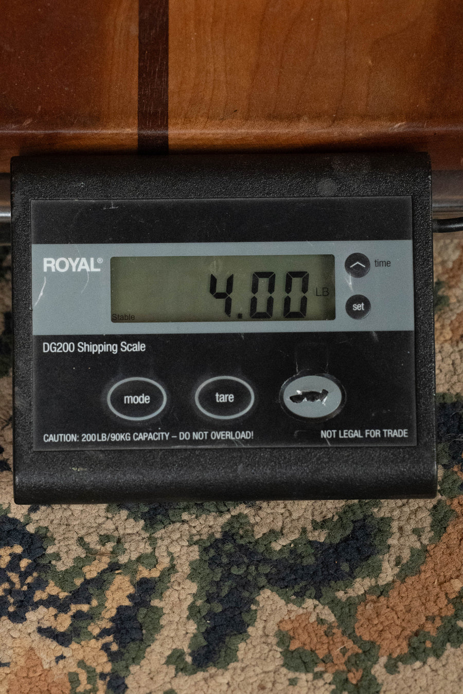 A digital shipping scale shows 4.00 lbs—ideal for shipping the Eastman Guitars E1OM All Solid Sitka/Sapele Acoustic Guitar #7765. The scale, with visible buttons and screen, rests on a patterned carpet.