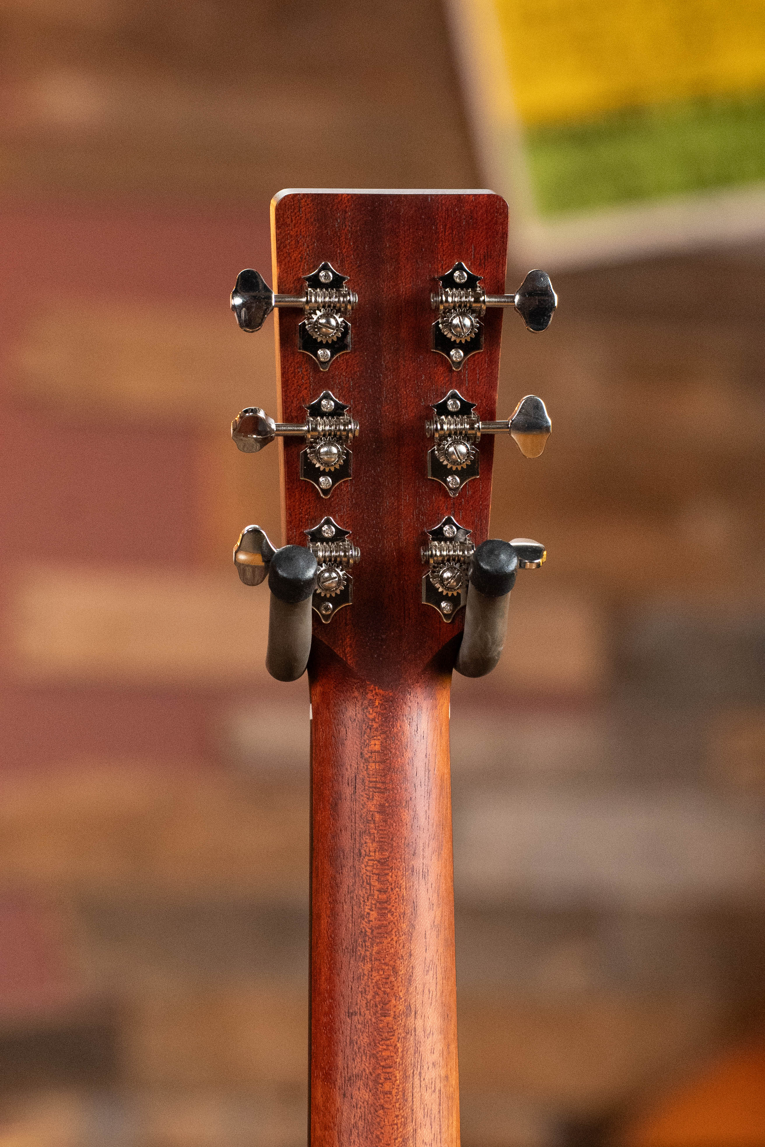 Close-up of the Eastman Guitars E1OM All Solid Sitka/Sapele Orchestra Model Acoustic Guitar #7102 headstock, featuring six tuning pegs and part of the wooden neck against a blurred, warm-toned background.