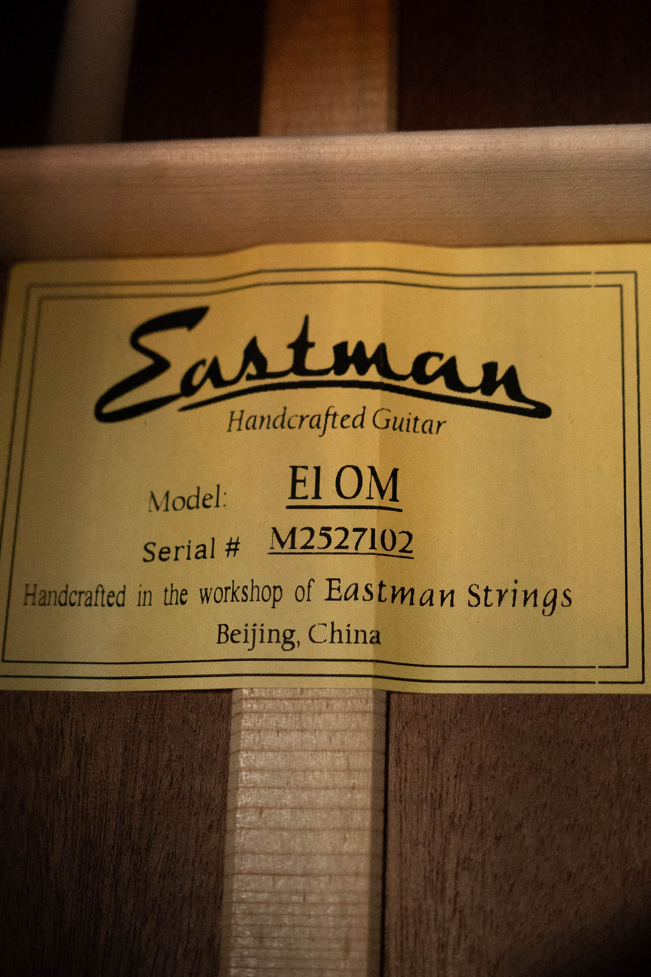 Close-up of a yellow label inside an Eastman Guitars E1OM All Solid Sitka/Sapele Orchestra Model Acoustic Guitar #7102, handcrafted in Beijing, China.