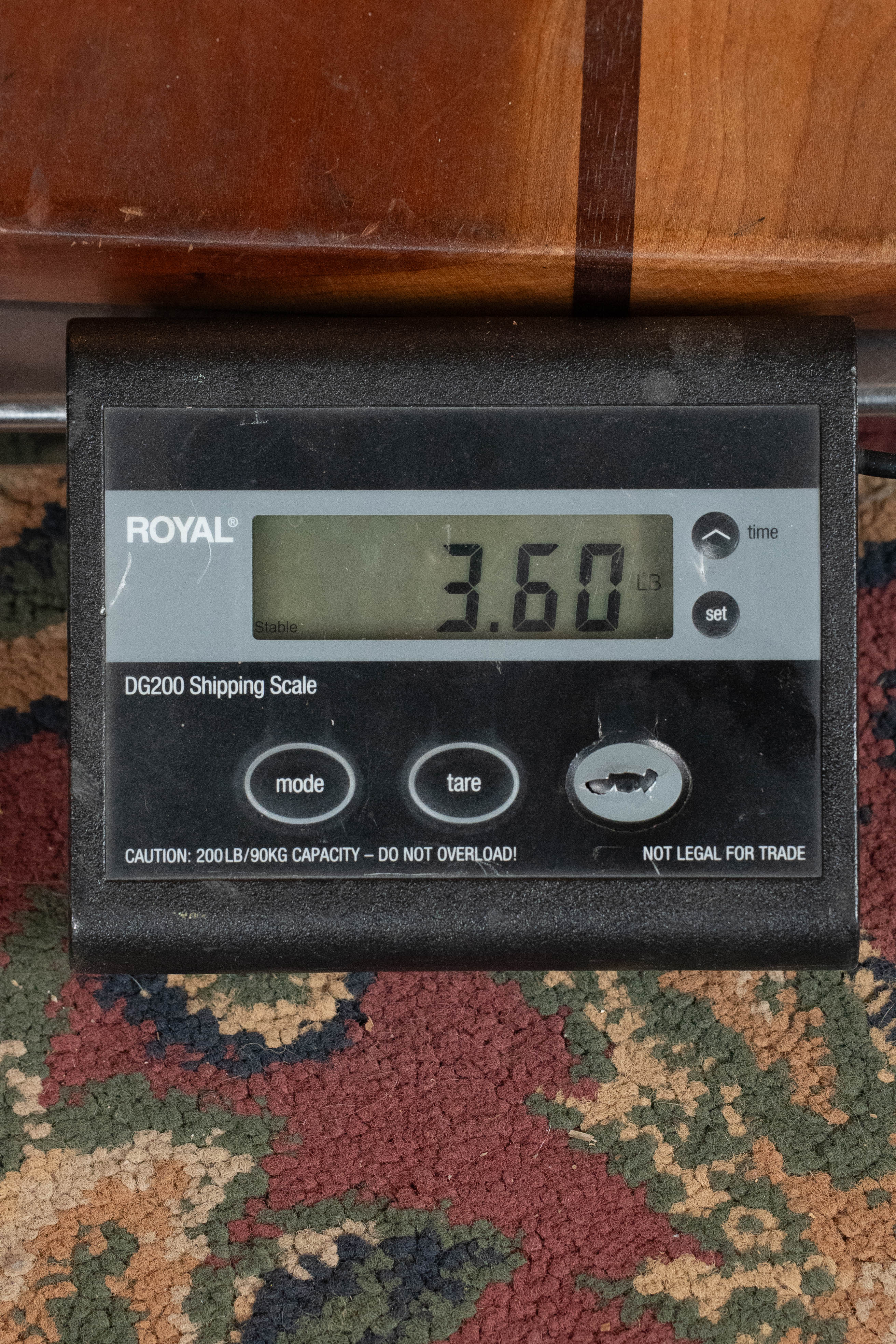 A digital Royal DG200 shipping scale displays 3.60 lbs on a patterned carpet under a wood surface—ideal for weighing the Eastman Guitars E1OM All Solid Sitka/Sapele Orchestra Model Acoustic Guitar #7102.
