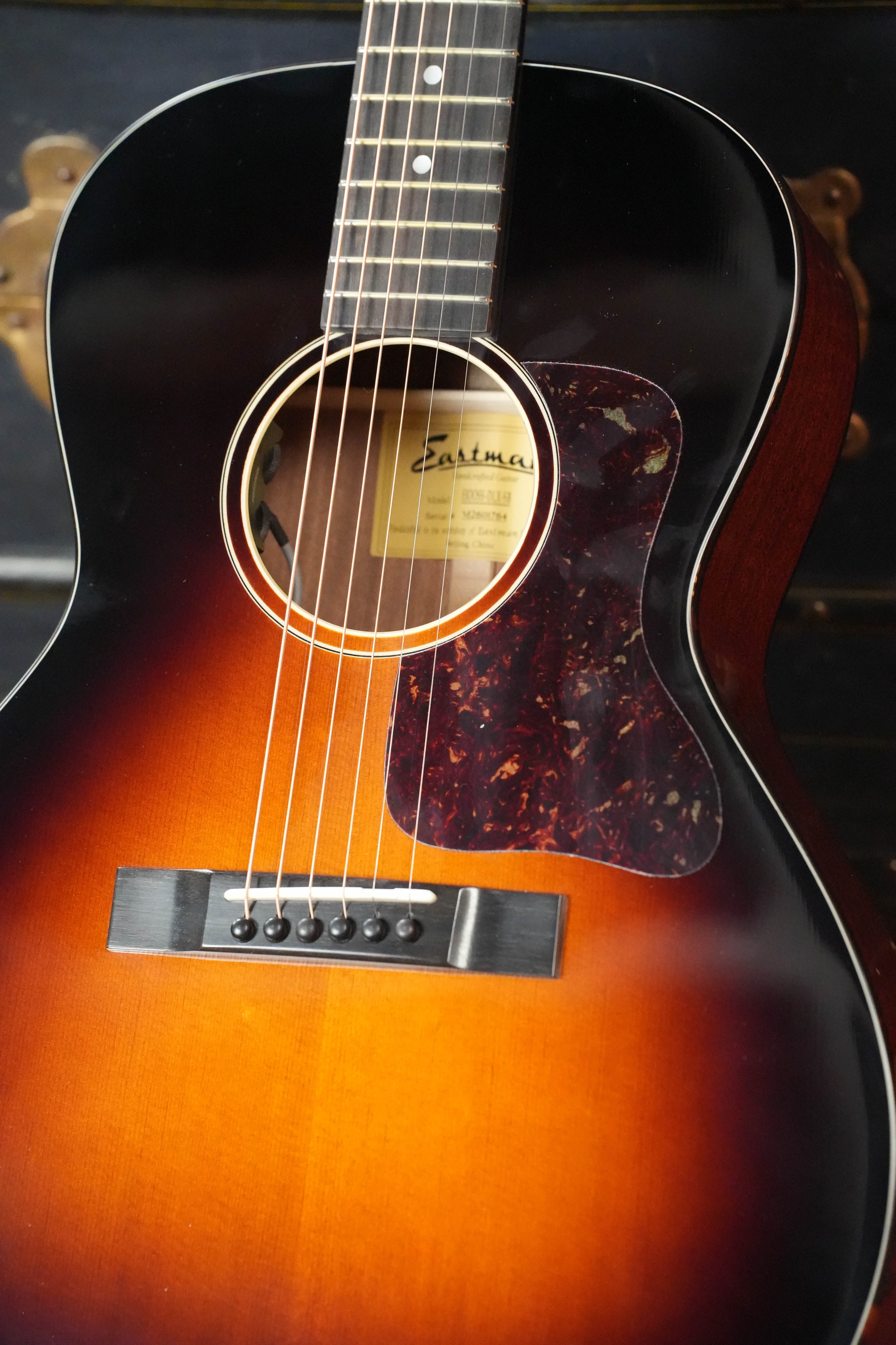 A close-up of the Eastman E1OOSS-DLX-SB Sunburst 00 Acoustic-Electric Guitar by Eastman Guitars shows its Truetone sunburst finish, strings, soundhole with label, tortoiseshell pickguard, mahogany neck, and part of the fretboard.