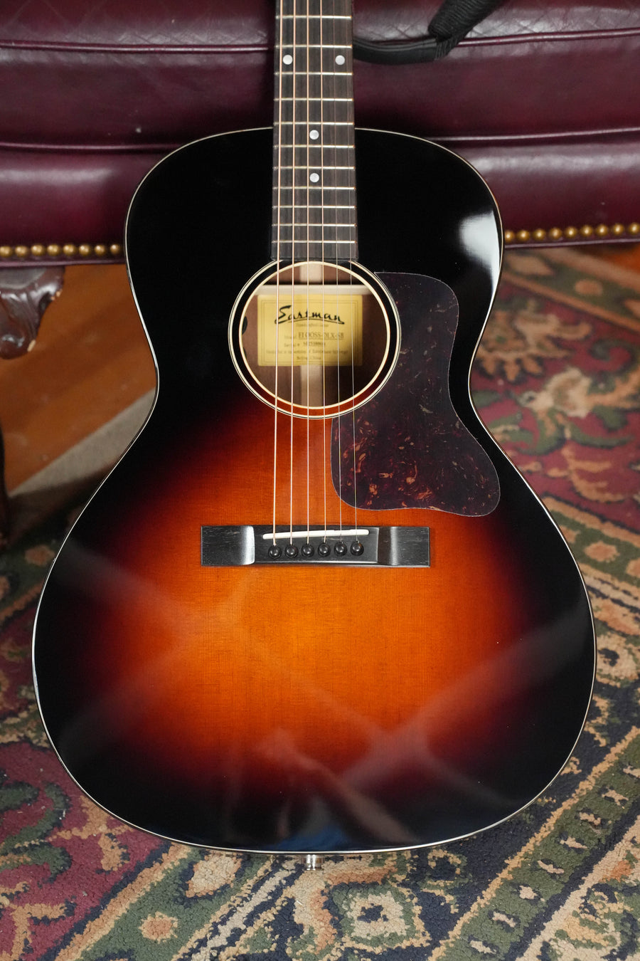 The Eastman E1OOSS-DLX-SB Sunburst 00 Acoustic-Electric Guitar #8804 by Eastman Guitars features a Truetone sunburst finish, six strings, and a tortoiseshell pickguard—classic pre-war vibes in a compact body.